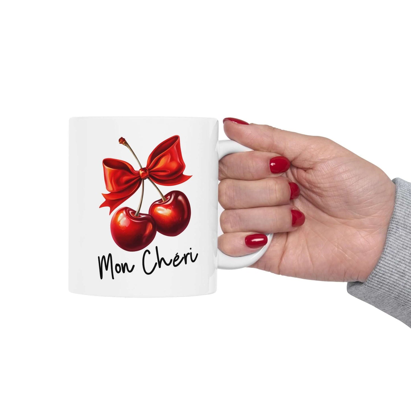 White ceramic mug held in hand, featuring two red cherries with a red bow and the text ‘Mon Chéri'.
