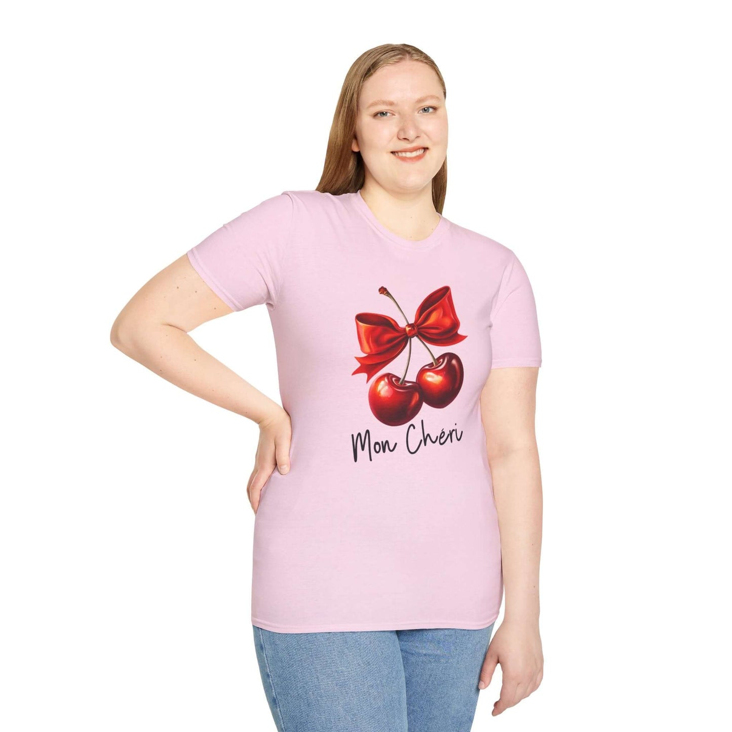 Smiling woman wearing a light pink unisex t-shirt featuring a stylish ‘Mon Chéri’ design with two vibrant red cherries tied with a bow and elegant text.