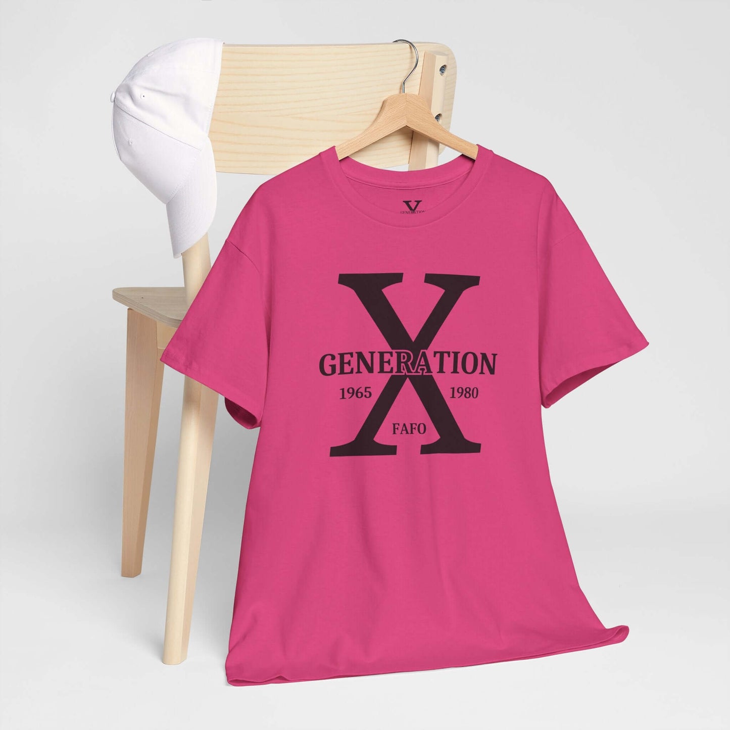 A pink t-shirt featuring a bold “GENERATION X” design with “FAFO” underneath is hanging on a wooden chair. A white baseball cap rests on the chair’s back, creating a stylish and casual display.