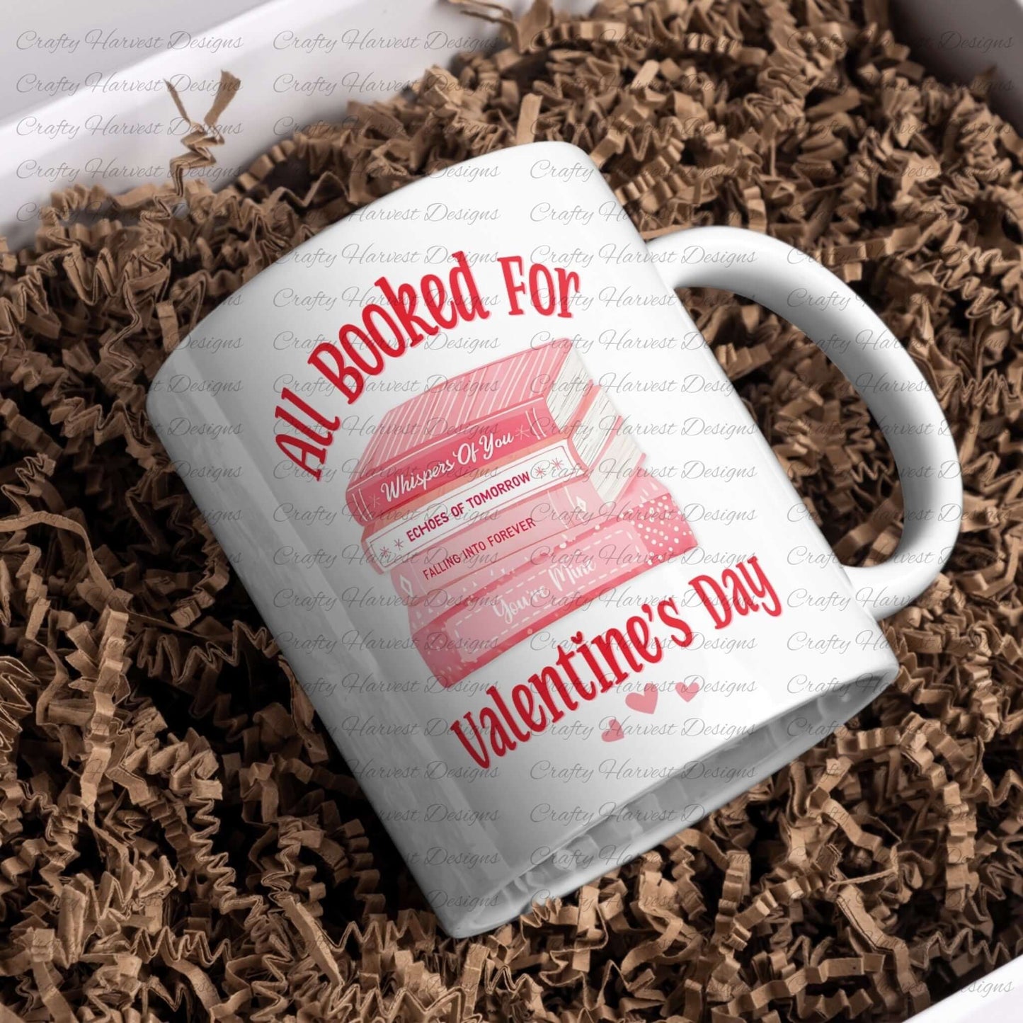 White ceramic mug featuring the ‘All Booked for Valentine’s Day’ design with a stack of pink books and romantic titles, surrounded by brown shredded paper packaging.