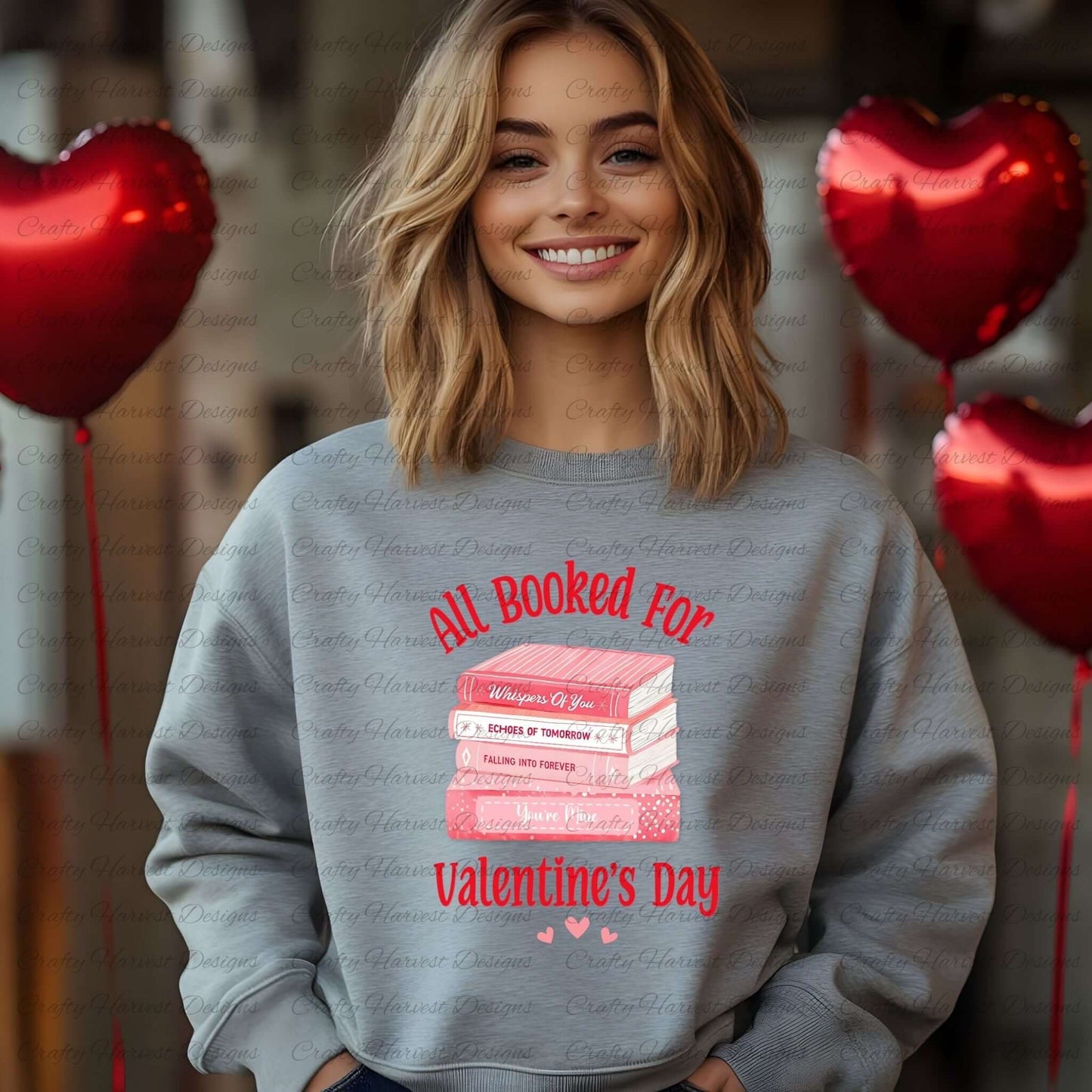 Smiling woman wearing a gray sweatshirt featuring the ‘All Booked for Valentine’s Day’ design with a stack of pink books and romantic titles, surrounded by red heart-shaped balloons.
