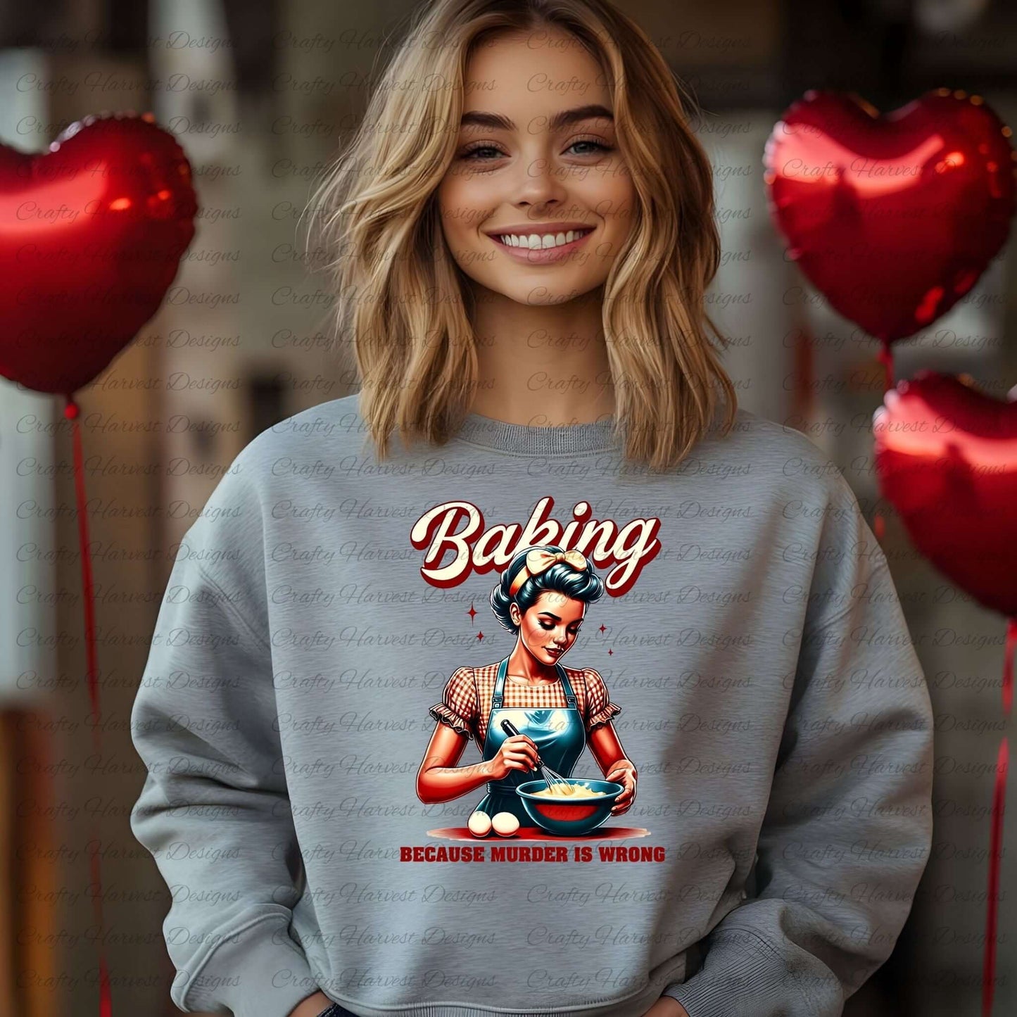 Smiling woman wearing a gray sweatshirt featuring a retro baking design with the phrase ‘Because Murder is Wrong,’ standing in front of red heart-shaped balloons.