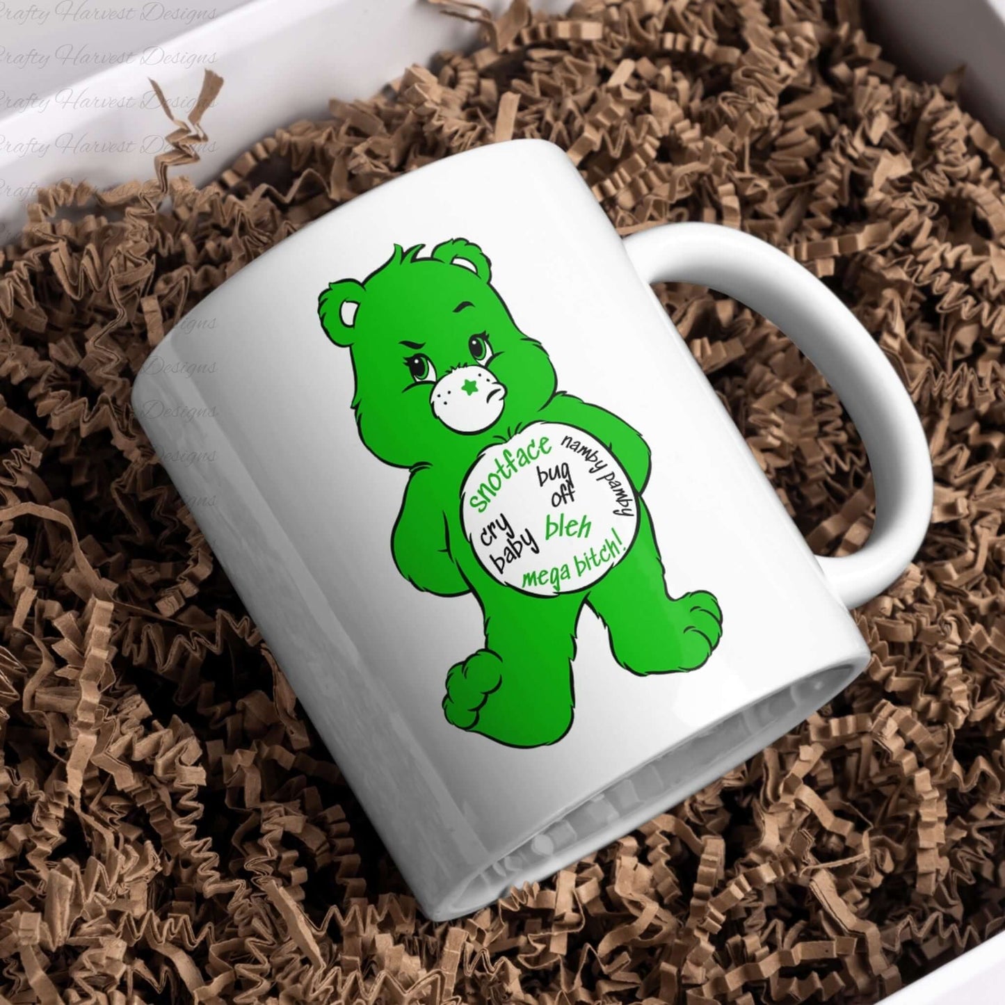 White mug mockup featuring the green Swear Bear with phrases like “Snotface,” “Namby Pamby,” “Bug Off,” and “Mega Bitch.” The mug is nestled in crinkle paper packaging.