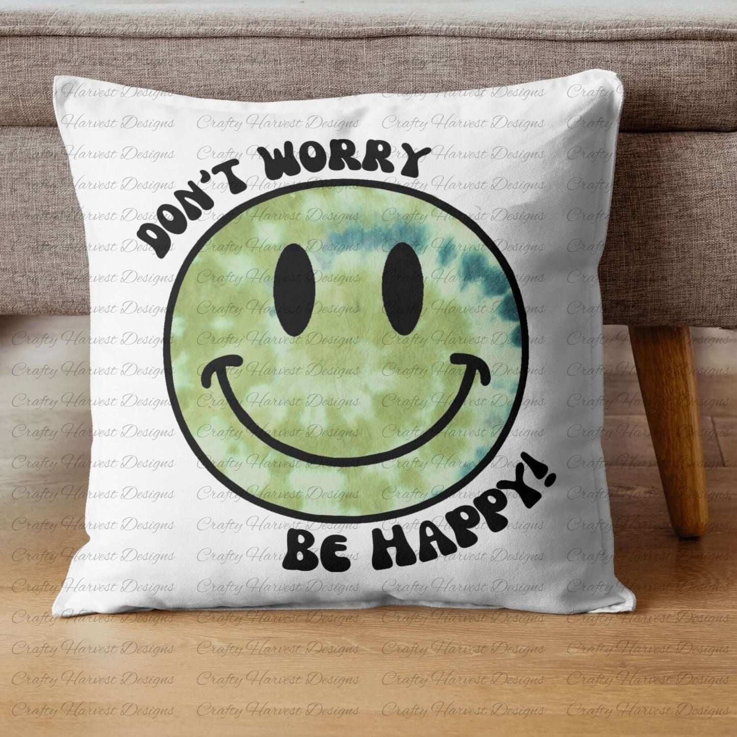 Square throw pillow resting against a couch, featuring a green tie-dye smiley face design with the phrase ‘Don’t Worry, Be Happy!’ in black text.