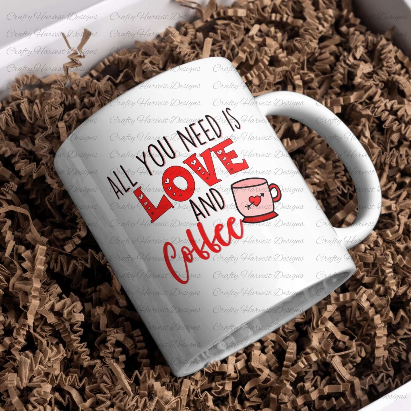 White ceramic mug featuring the All You Need is Love and Coffee design in red and black, with a coffee cup graphic and heart detail, nestled in shredded kraft paper packaging