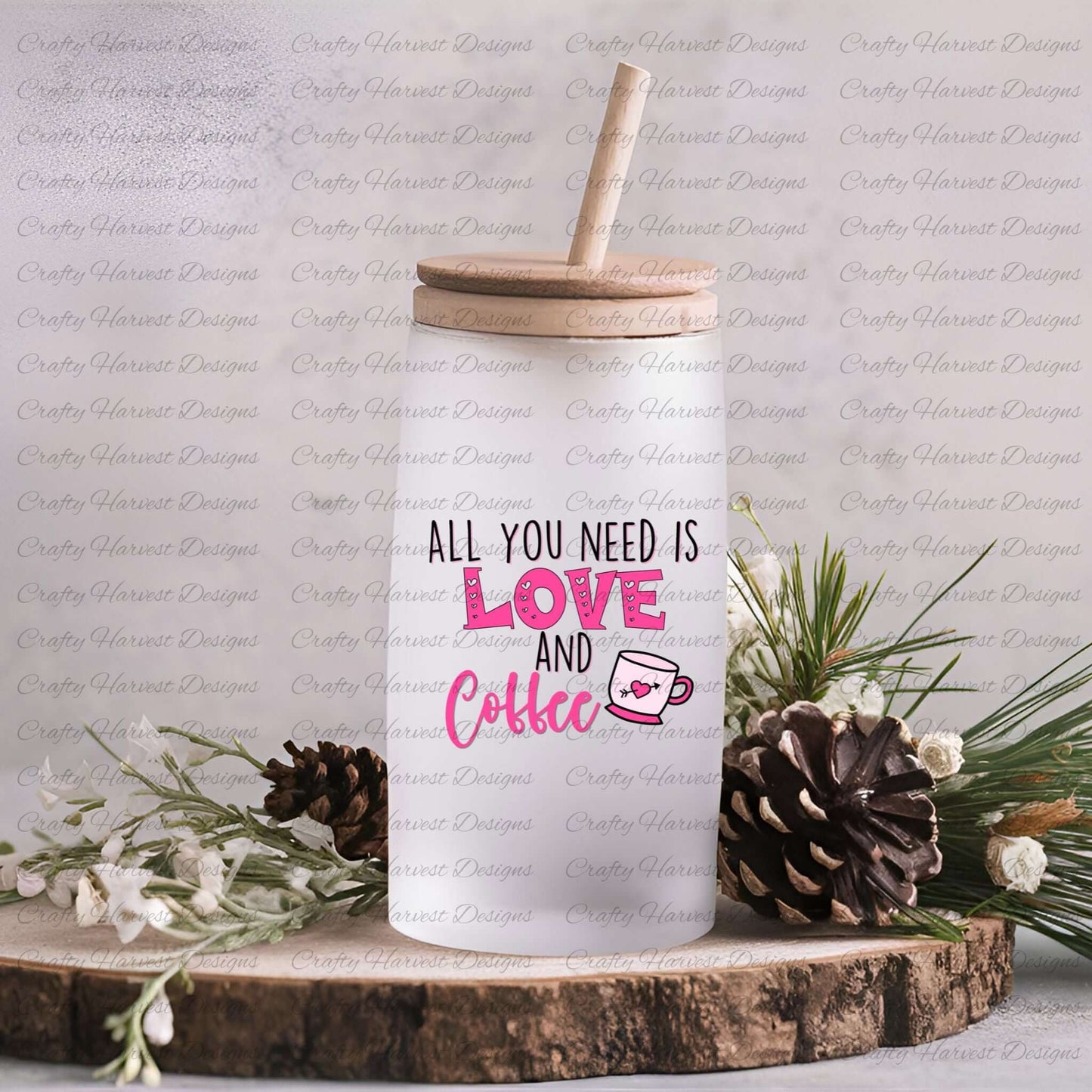 Tall frosted glass can with a wooden lid, featuring the All You Need is Love and Coffee design in pink and black, with a pink coffee cup graphic and heart detail, displayed on a rustic wood slice with pinecones, white flowers, and greenery accents.