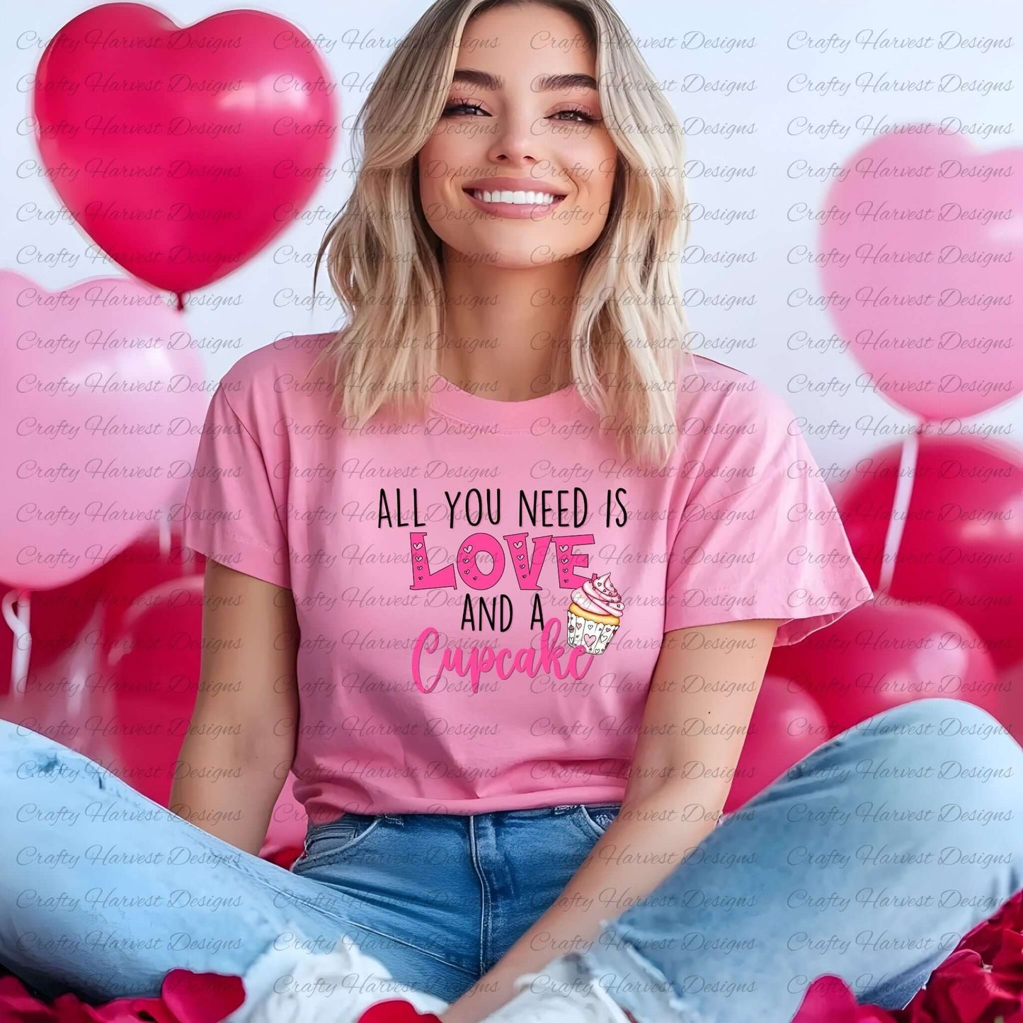 Woman wearing a pink t-shirt featuring the All You Need is Love and a Cupcake design in pink with a cupcake graphic, sitting in front of pink heart balloons.