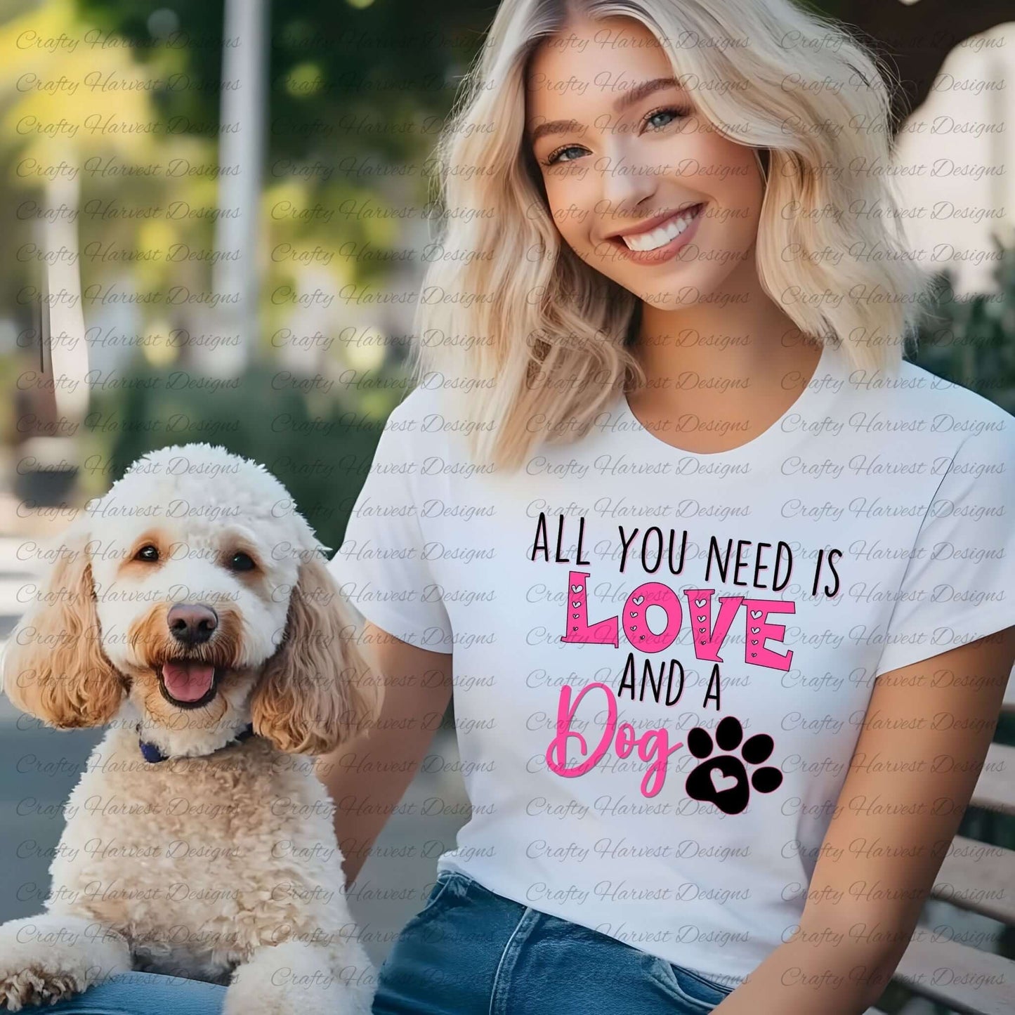 Woman wearing a white t-shirt featuring the All You Need is Love and a Dog design in pink and black with a paw print graphic, sitting next to a happy golden doodle dog.