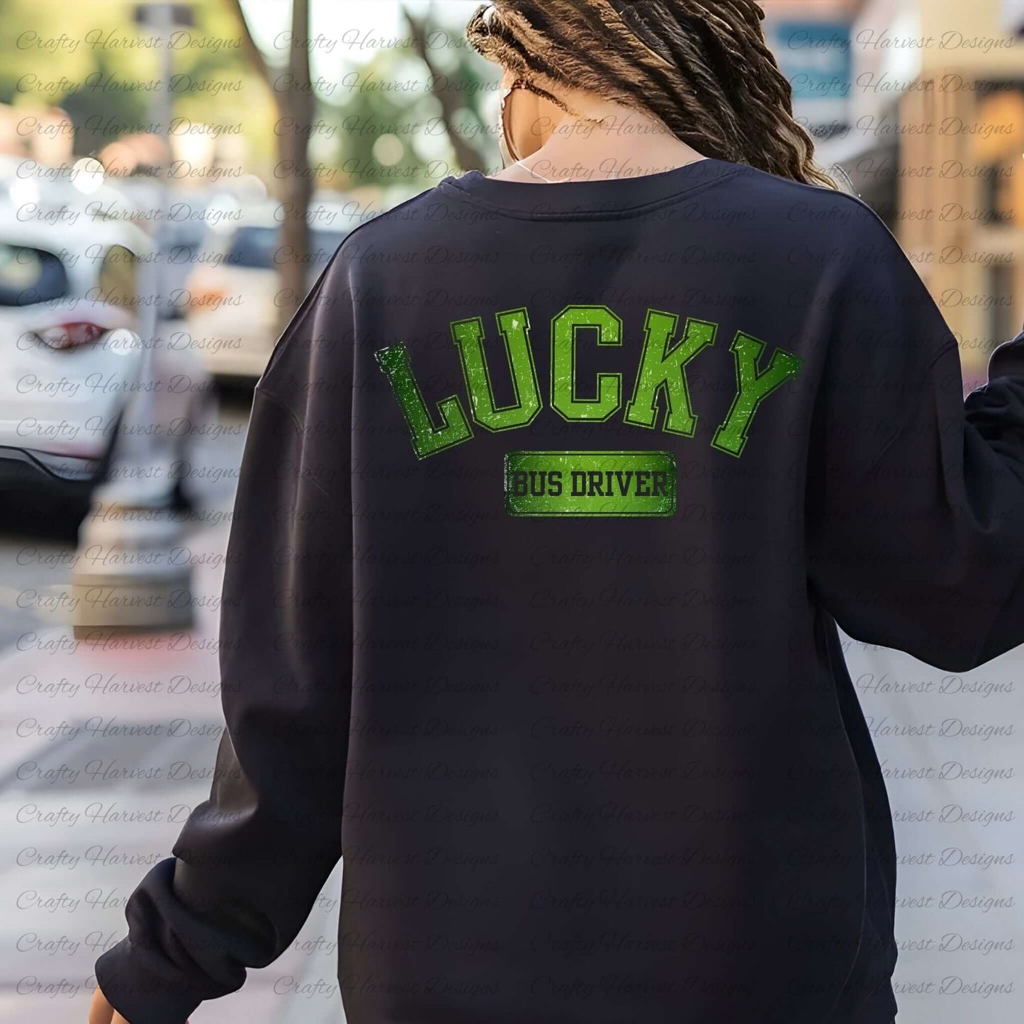 Rear view of a woman wearing a black sweatshirt with the ‘Lucky Bus Driver’ St. Patrick’s Day design in bold green text. The background shows an outdoor street setting with trees and cars blurred in the distance.