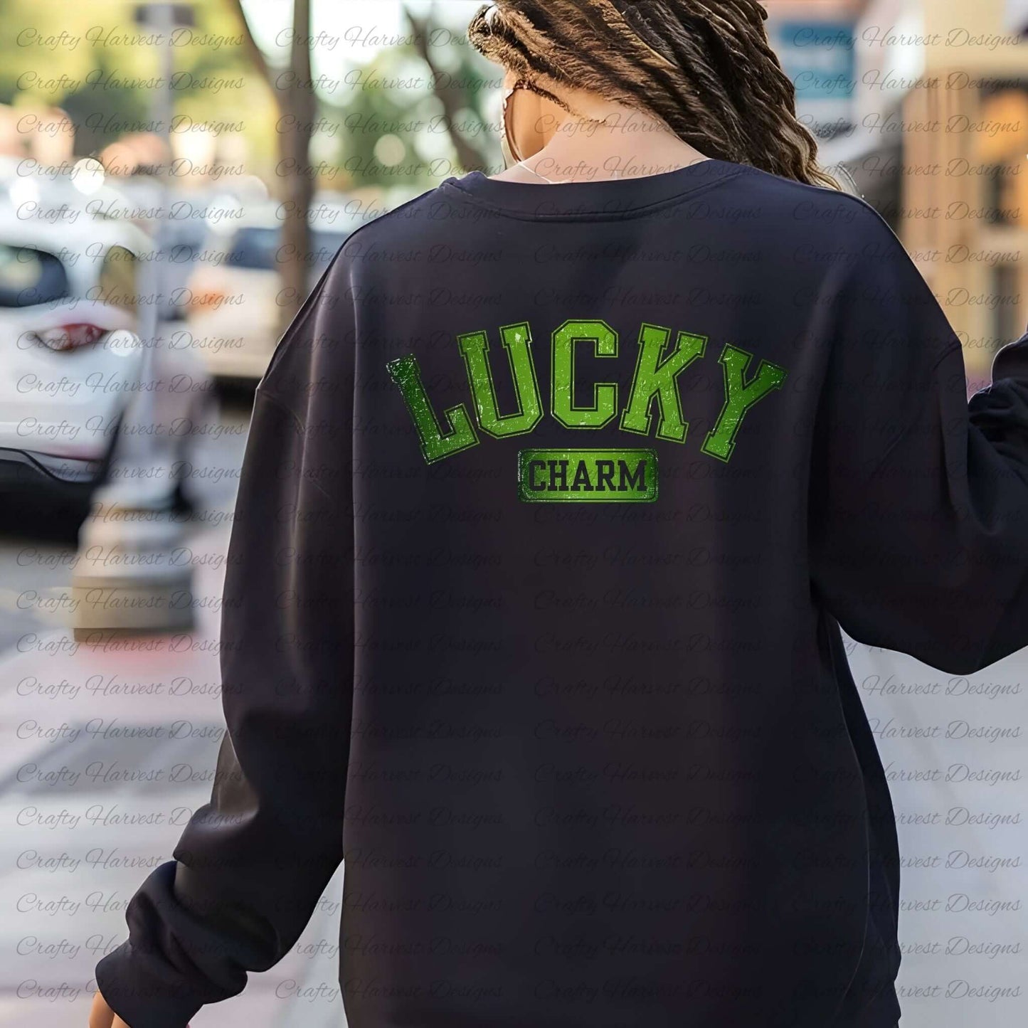Rear view of a woman wearing a black sweatshirt with the ‘Lucky Charm’ St. Patrick’s Day design in bold green text. The background shows an outdoor street setting with blurred cars and trees.