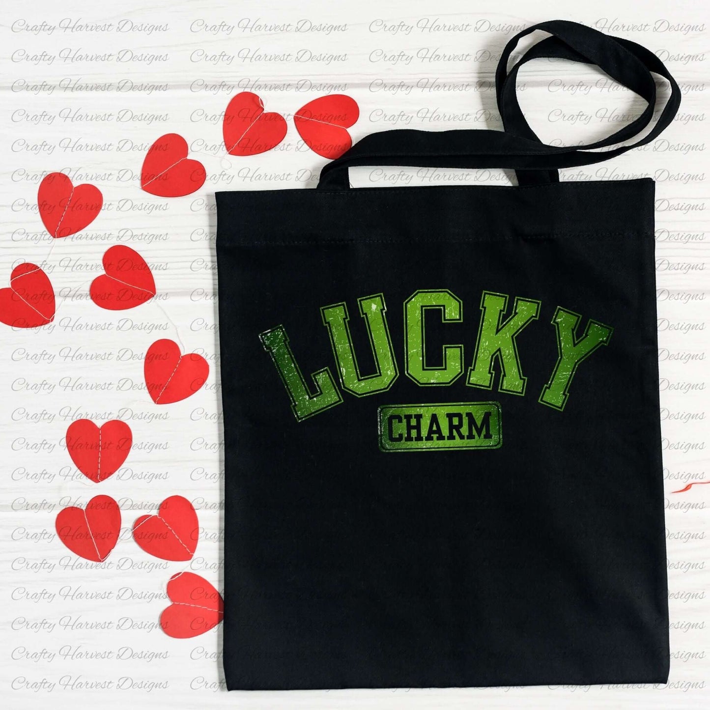 Black tote bag featuring the ‘Lucky Charm’ St. Patrick’s Day design in bold green text. The bag is displayed on a white surface decorated with red heart-shaped cutouts.