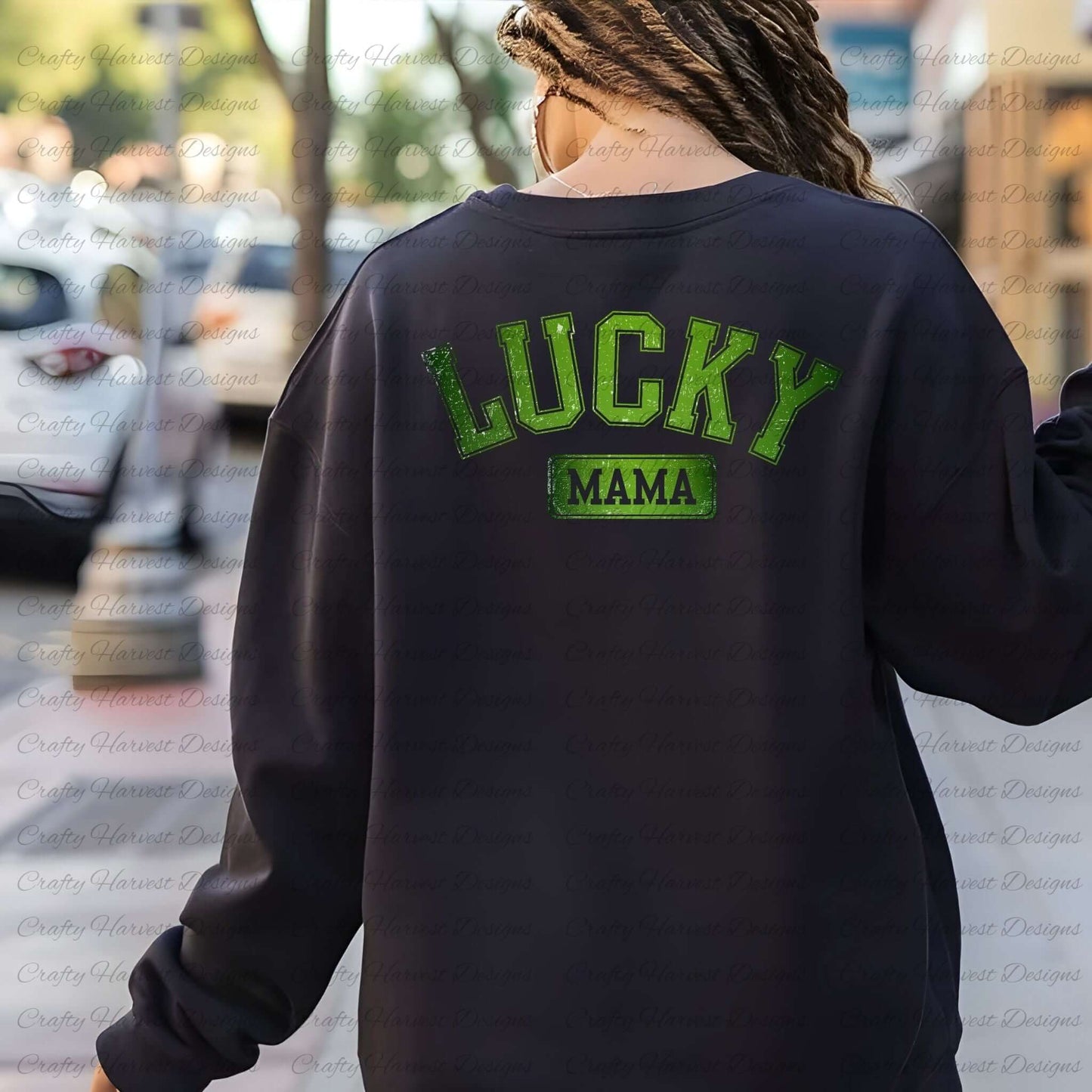 Rear view of a woman wearing a black sweatshirt with the ‘Lucky Mama’ St. Patrick’s Day design in bold green text. The background features an outdoor street setting with blurred trees and parked cars.