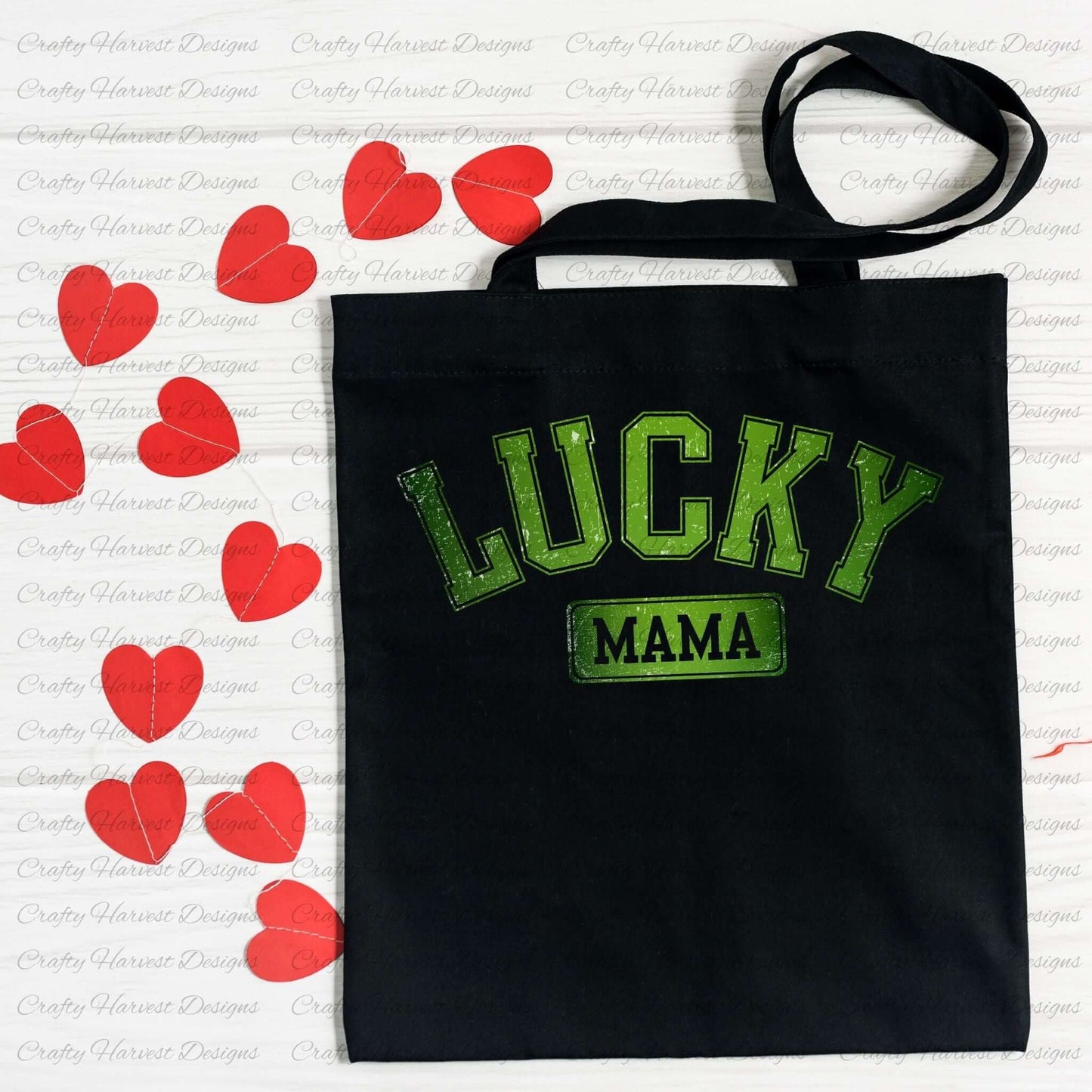 Black tote bag featuring the ‘Lucky Mama’ St. Patrick’s Day design in bold green text. The bag is displayed on a white surface decorated with red heart-shaped cutouts.