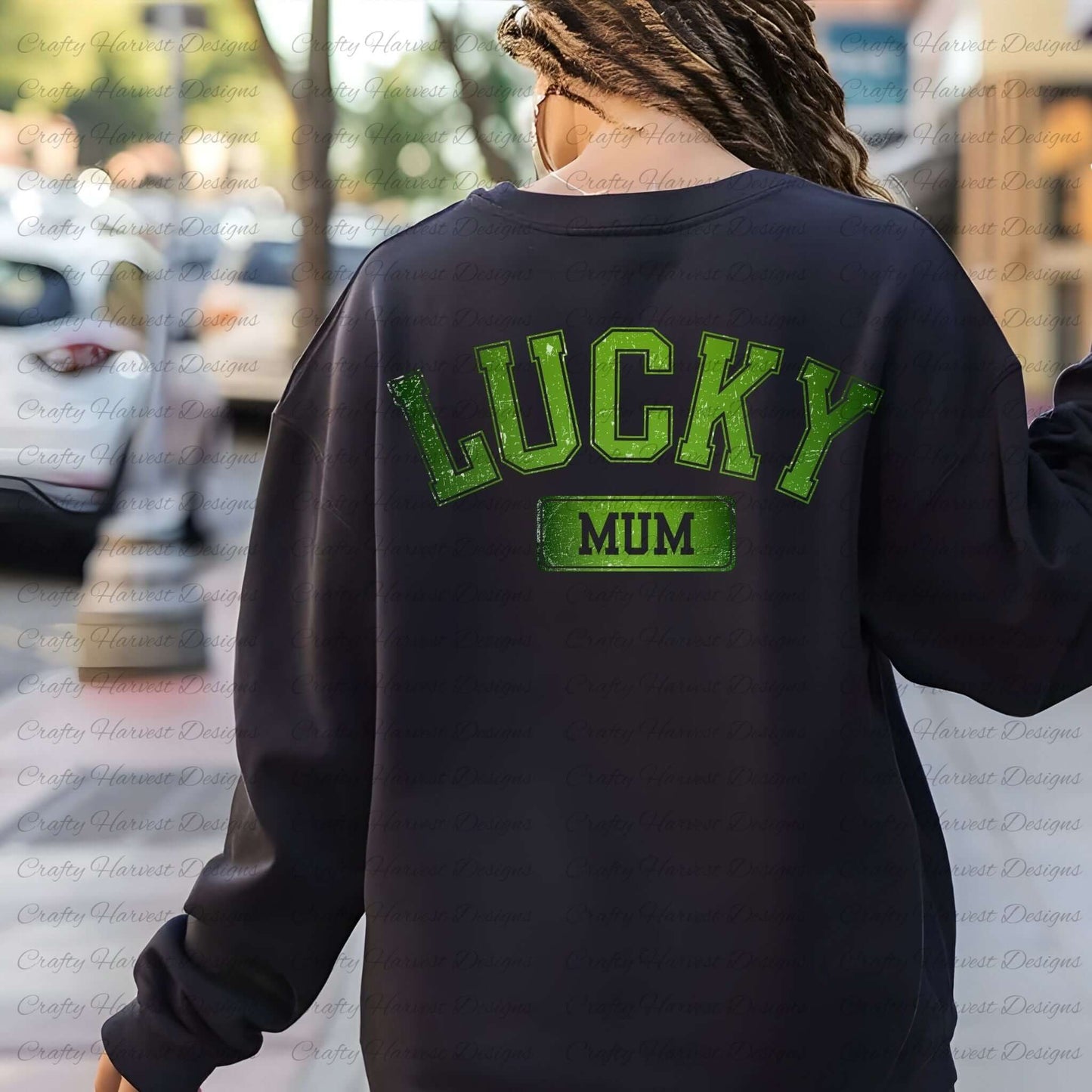Rear view of a woman wearing a black sweatshirt with the ‘Lucky Mum’ St. Patrick’s Day design in bold green text. The background features an outdoor street setting with blurred trees and parked cars.