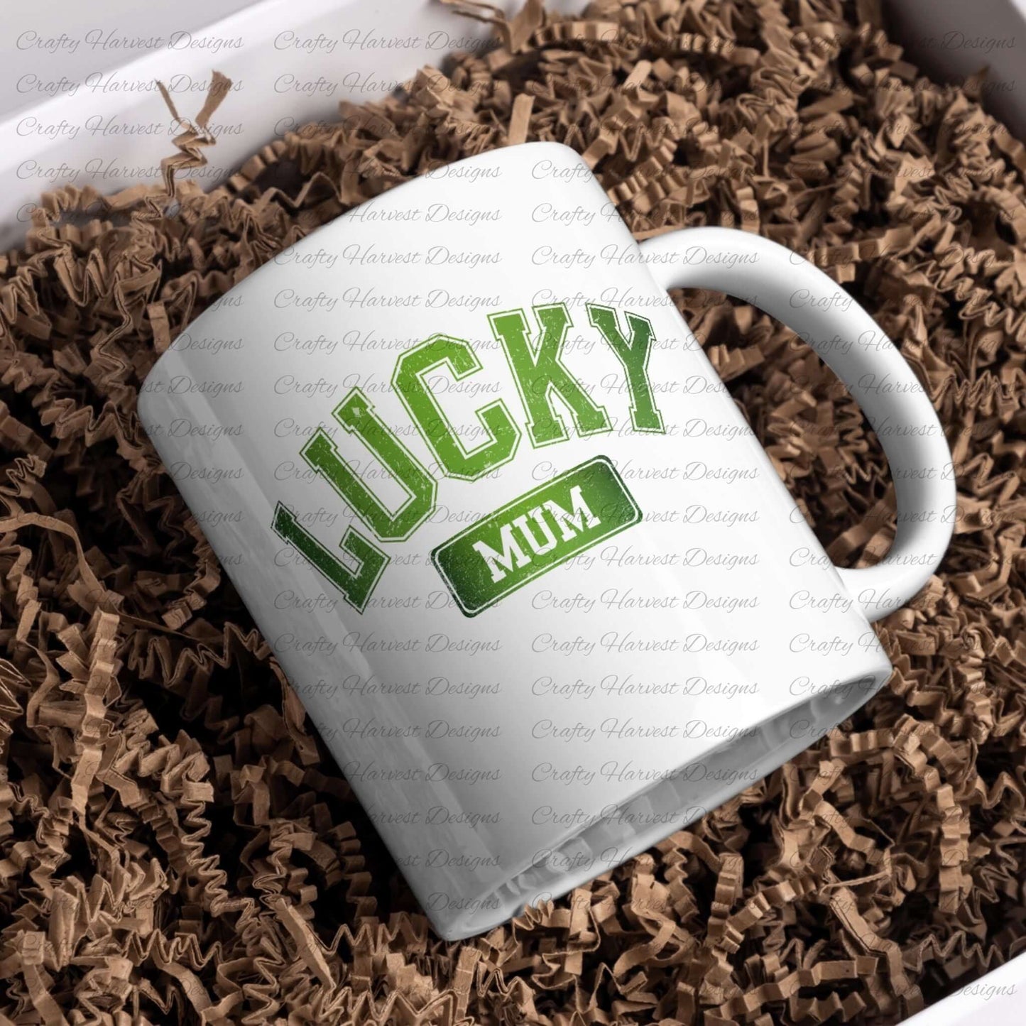 White ceramic mug featuring the ‘Lucky Mum’ St. Patrick’s Day design in bold green text. The mug is placed on a bed of brown crinkle paper for a festive presentation.