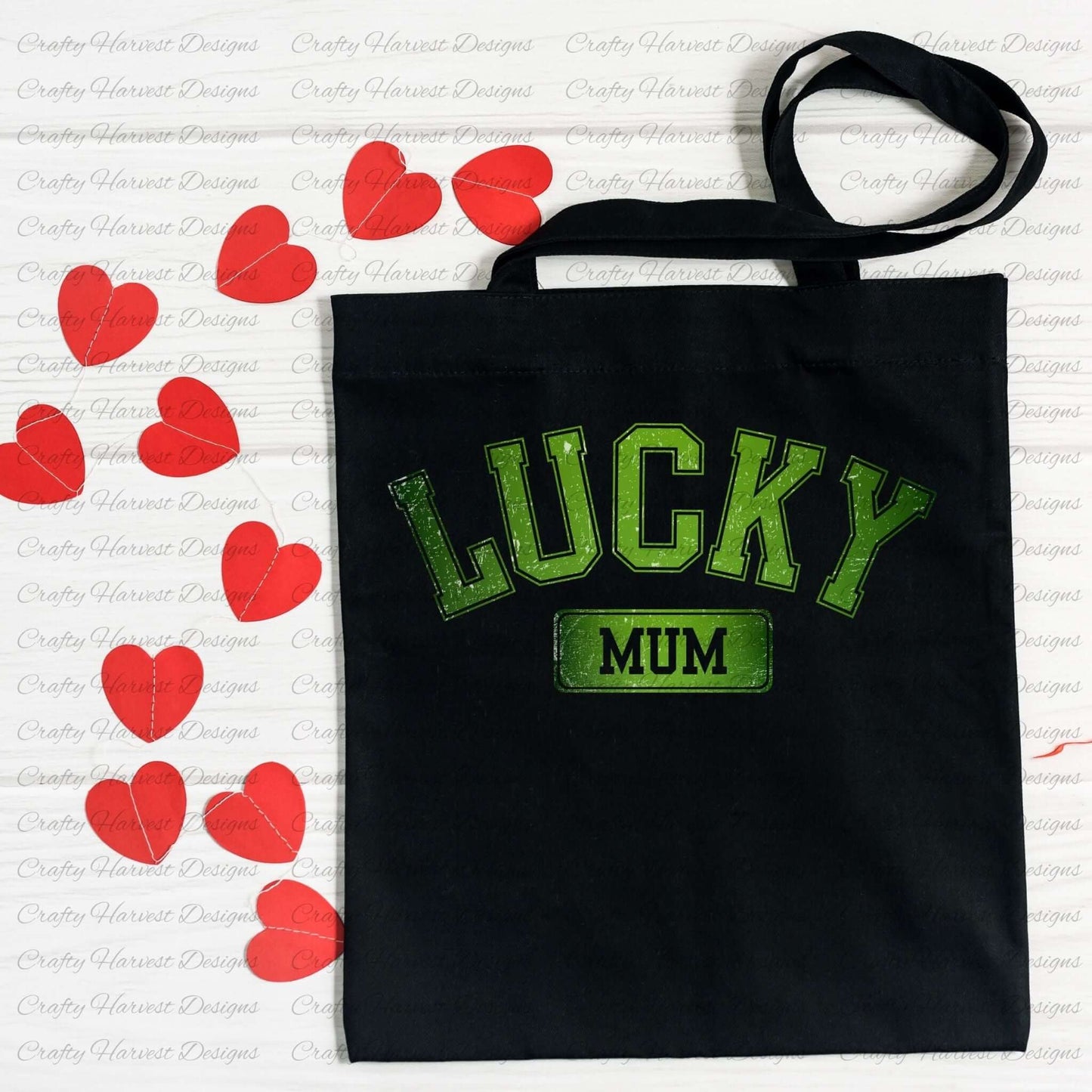 Black tote bag featuring the ‘Lucky Mum’ St. Patrick’s Day design in bold green text. The bag is displayed on a white surface decorated with red heart-shaped cutouts.