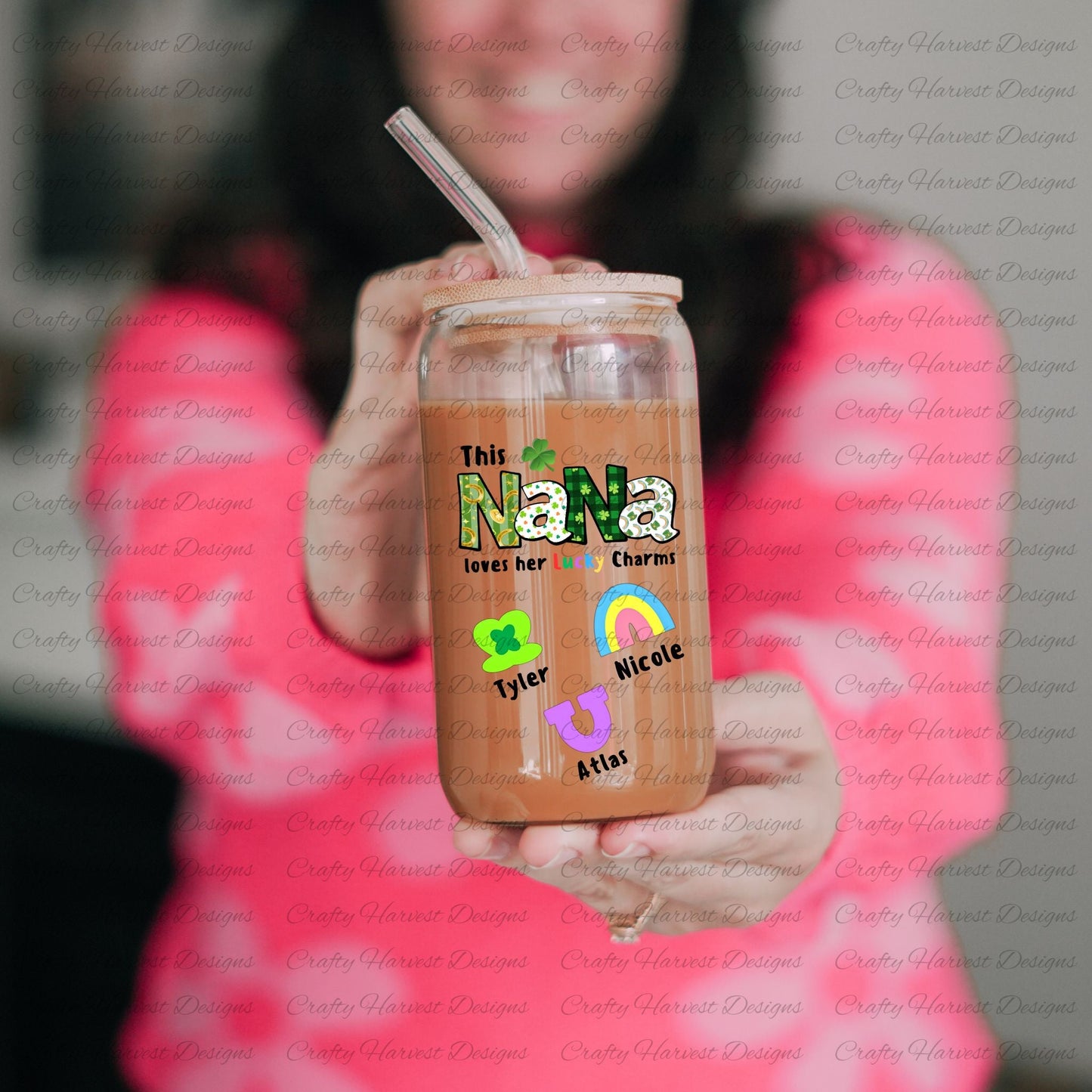 Person holding a glass can with a bamboo lid and straw, featuring a “This NANA loves her Lucky Charms” design with green-patterned letters and two colorful charm icons with the names “Emily” and “Thomas” below them.