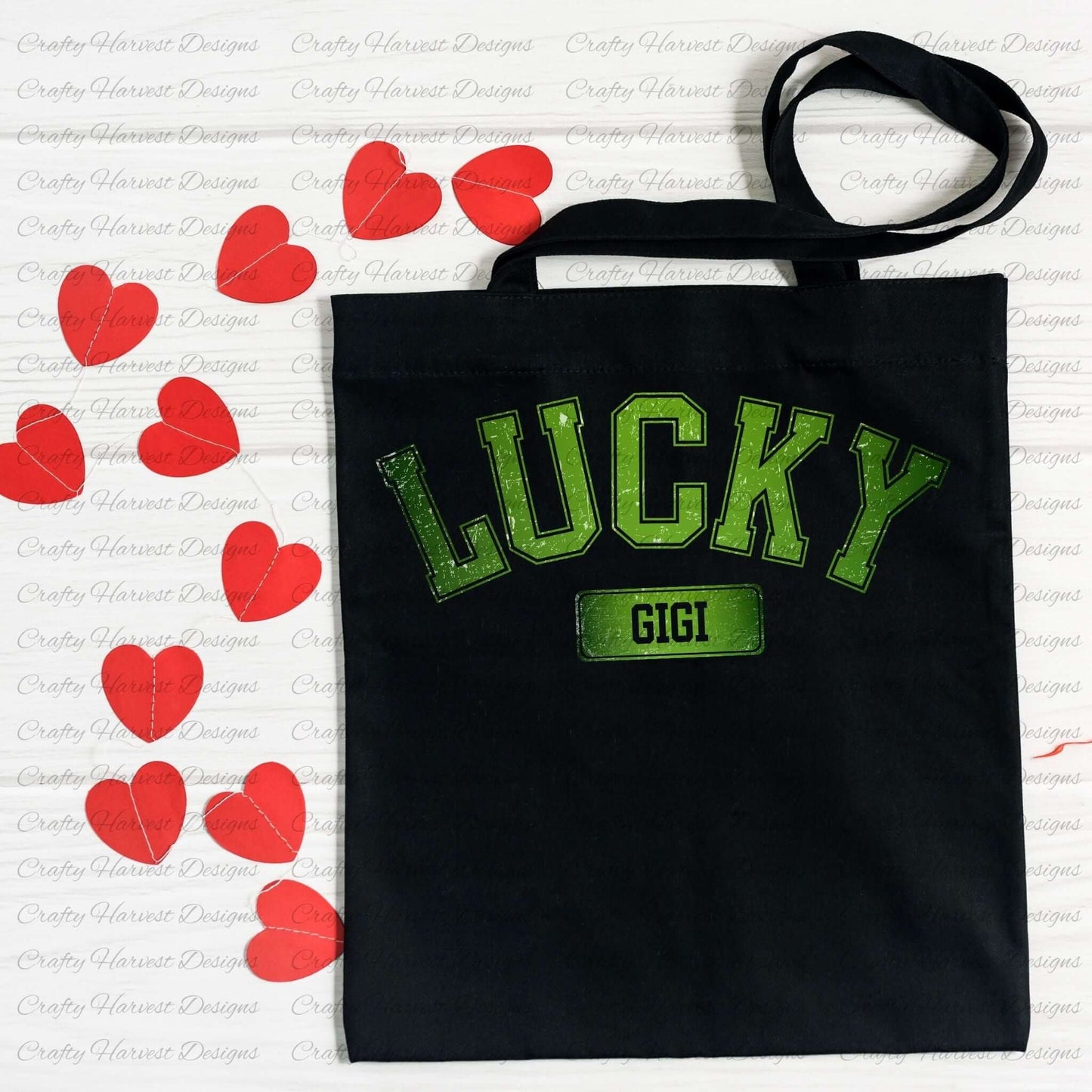 Black tote bag featuring the ‘Lucky Gigi’ St. Patrick’s Day design in bold green text. The bag is displayed on a white surface decorated with red heart-shaped cutouts.