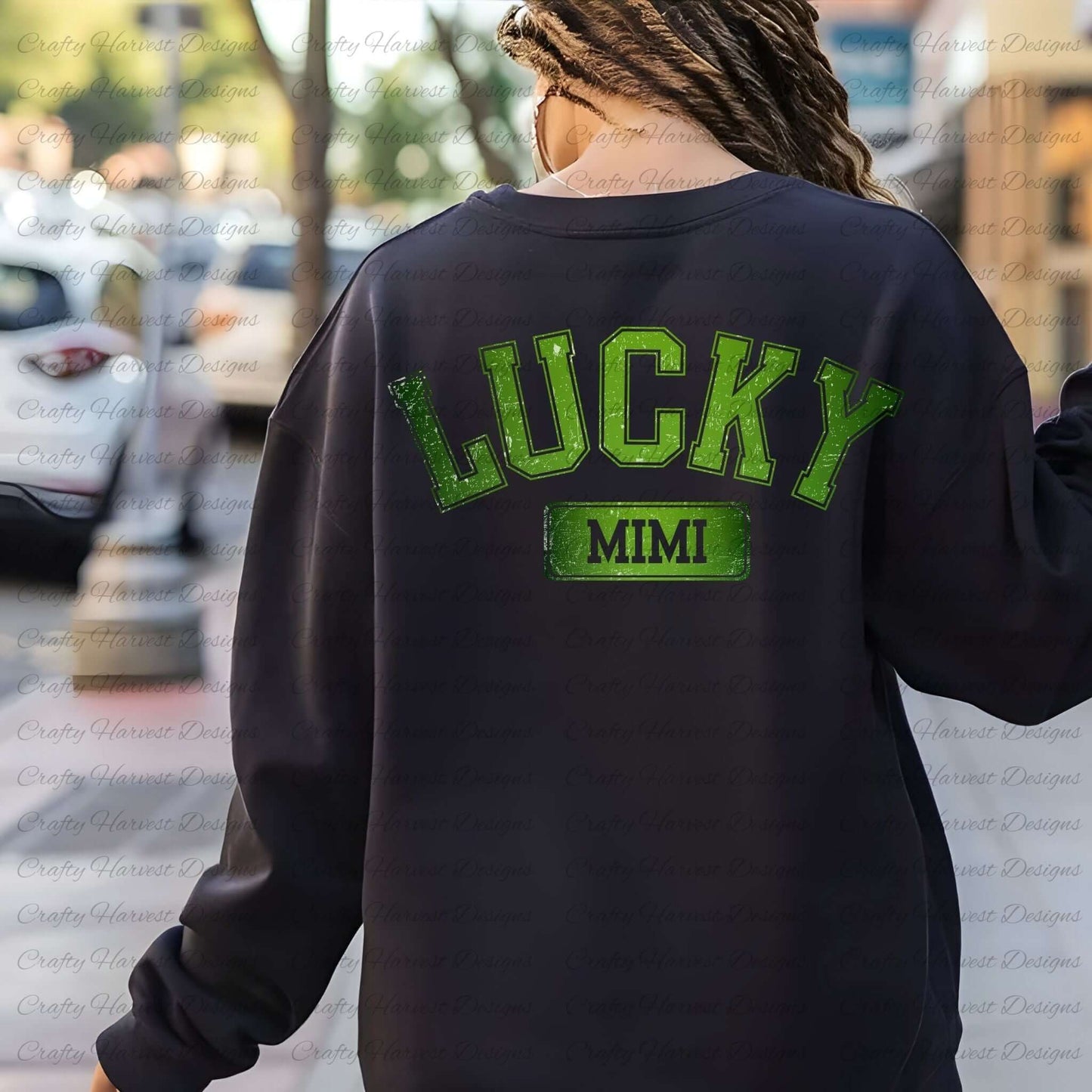 Rear view of a woman wearing a black sweatshirt featuring the design ‘Lucky Mimi’ in bold green text with a festive St. Patrick’s Day theme. She is walking outdoors with a blurred street and trees in the background.