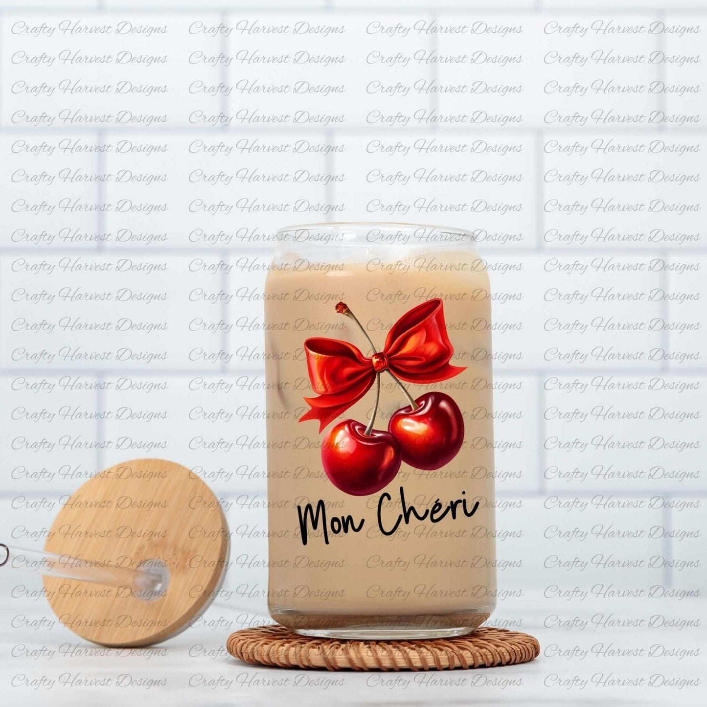 Clear glass can featuring a digital design of two vibrant red cherries tied with a bold red bow, accompanied by the elegant black text ‘Mon Chéri.’ The glass can is displayed on a woven coaster alongside a wooden lid with a straw slot, emphasizing its use as a trendy and functional beverage container.