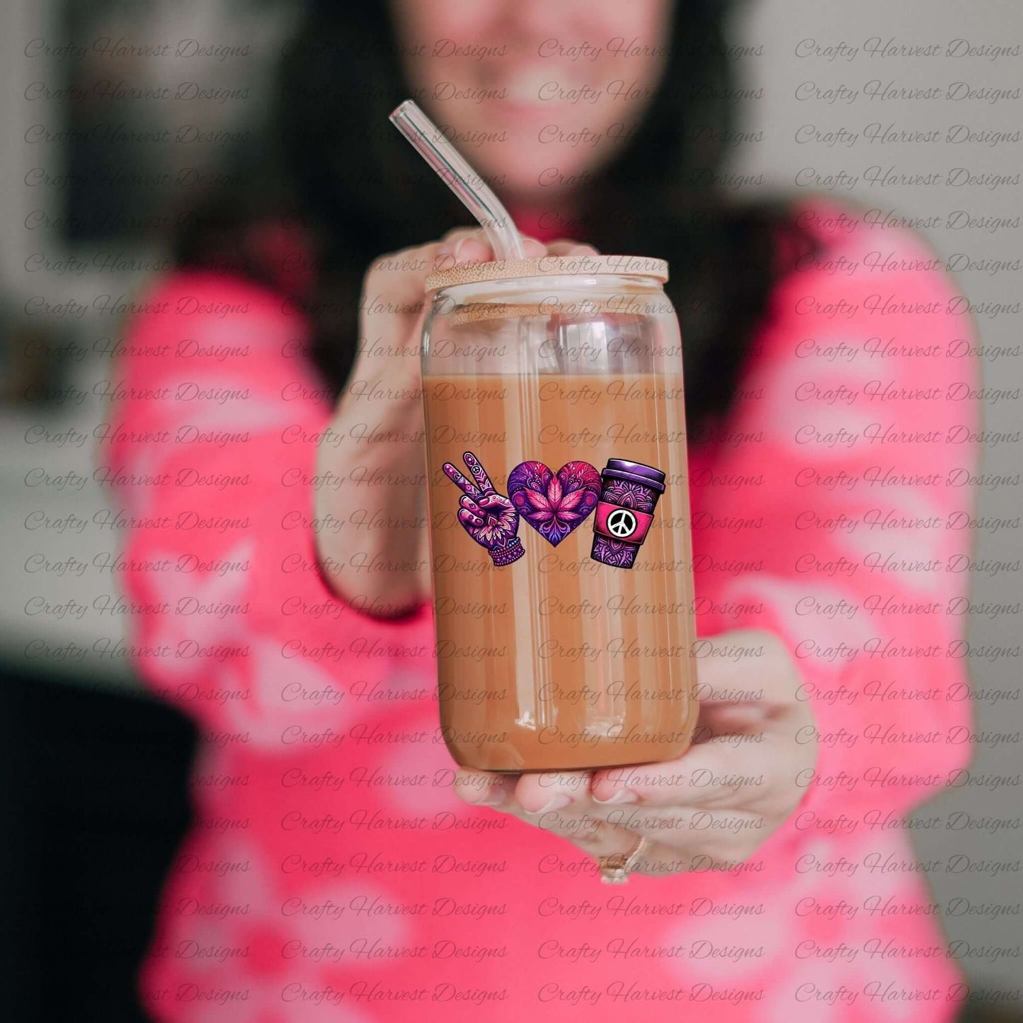 Glass can cup with a bamboo lid and straw, featuring a peace-themed design in vibrant purple and pink tones. Includes a peace sign hand, a heart with intricate floral patterns, and a coffee cup with a peace symbol, held by a person wearing a pink sweater.