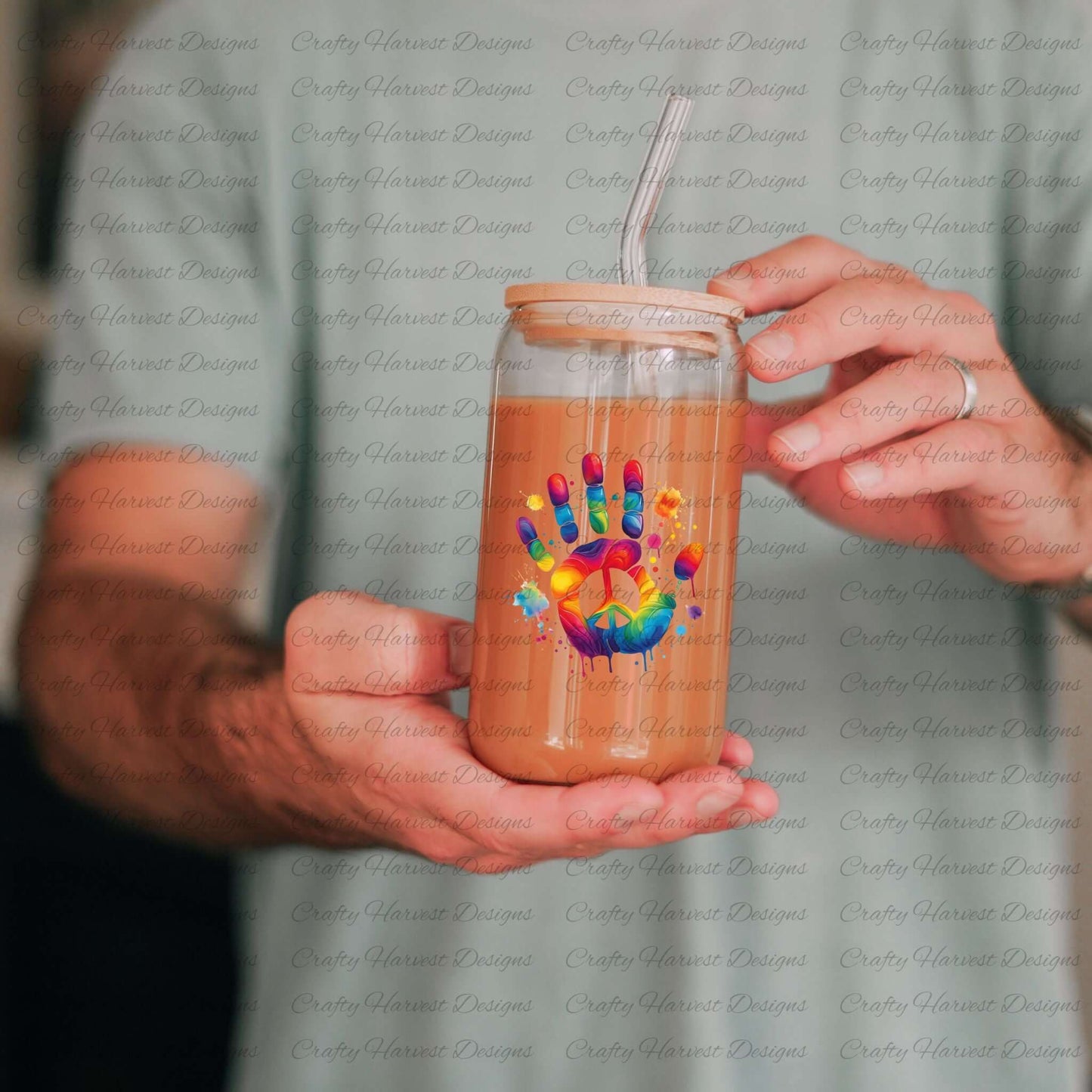 Glass can with wooden lid and straw, featuring a rainbow dripping paint handprint with a peace symbol. Printed drinkware mockup held by a person.