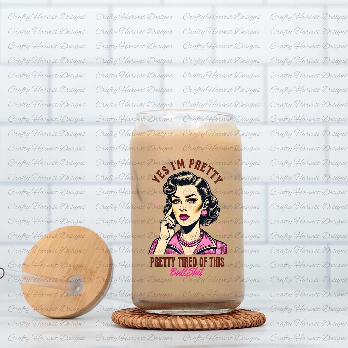 Clear glass can featuring a retro-inspired digital design of a vintage-style woman with the humorous text ‘Yes I’m Pretty - Pretty Tired of This Bullsh*t’ in pink and brown colors. The glass can is displayed on a woven coaster alongside a wooden lid with a straw slot, emphasizing its use as a trendy and functional beverage container.