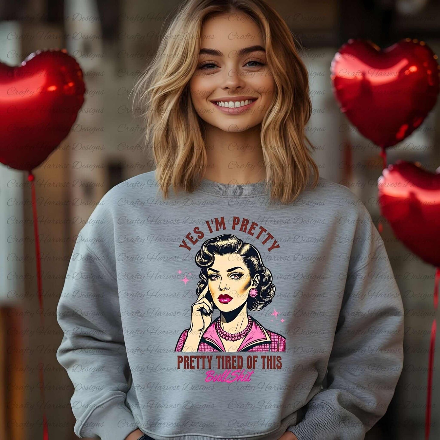 Smiling woman wearing a gray sweatshirt featuring a retro-inspired digital design of a vintage-style woman with the humorous text ‘Yes I’m Pretty - Pretty Tired of This Bullsh*t’ in pink and brown colors. Red heart-shaped balloons are visible in the background, adding a playful and cheeky vibe to the design.