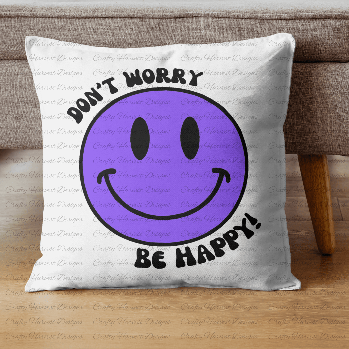Square throw pillow resting against a couch, featuring a purple smiley face design with the phrase ‘Don’t Worry, Be Happy!’ in black text.