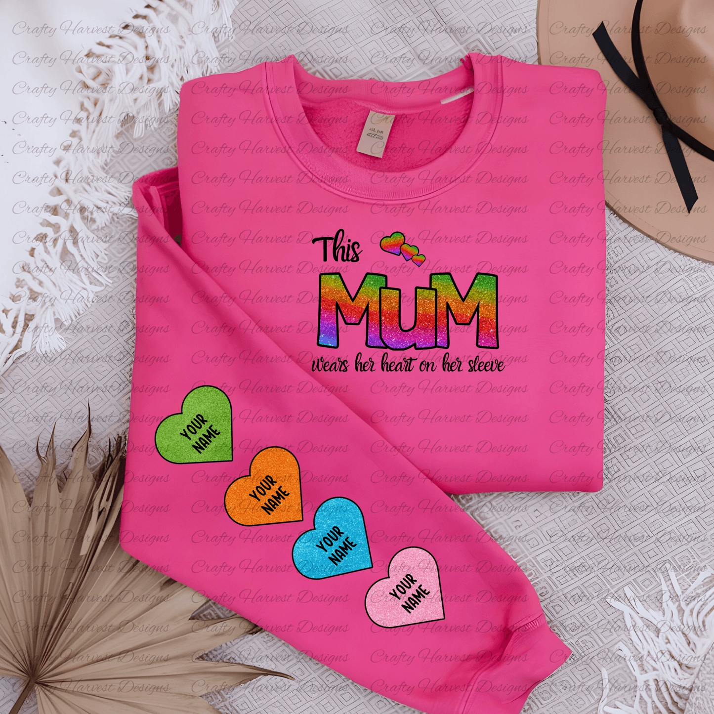 Mockup of a pink t-shirt featuring the “This Mum Wears Her Heart on Her Sleeve” design in a colorful rainbow glitter style. The sleeve displays four customizable heart accents in green, orange, blue, and pink glitter patterns with the placeholder text “Your Name.” The t-shirt is styled with soft, neutral decor for a cozy presentation.