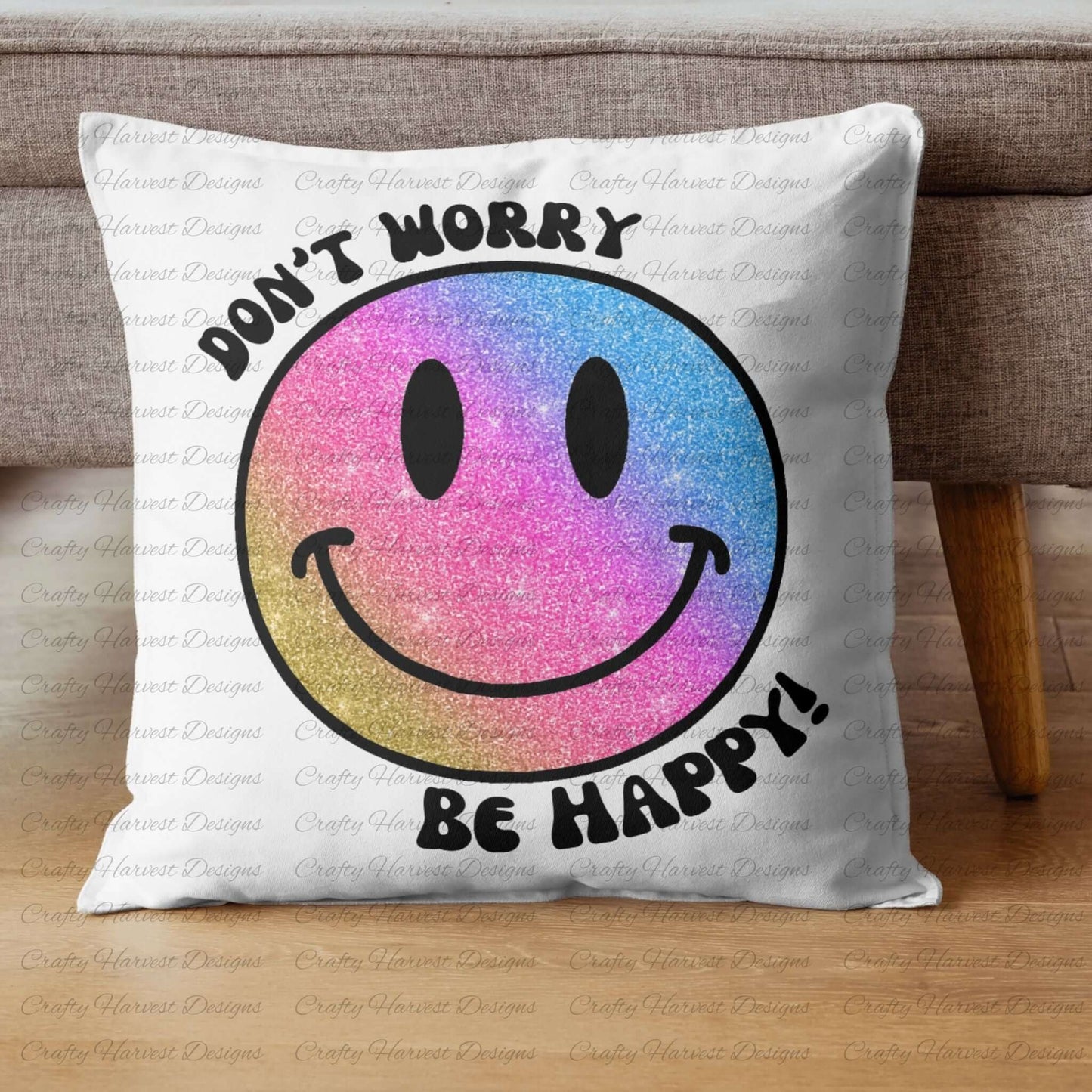 Square throw pillow resting against a couch, featuring a glitter gradient smiley face design with the phrase ‘Don’t Worry, Be Happy!’ in black text. The smiley face transitions from pink to blue to gold, creating a vibrant and cheerful look.