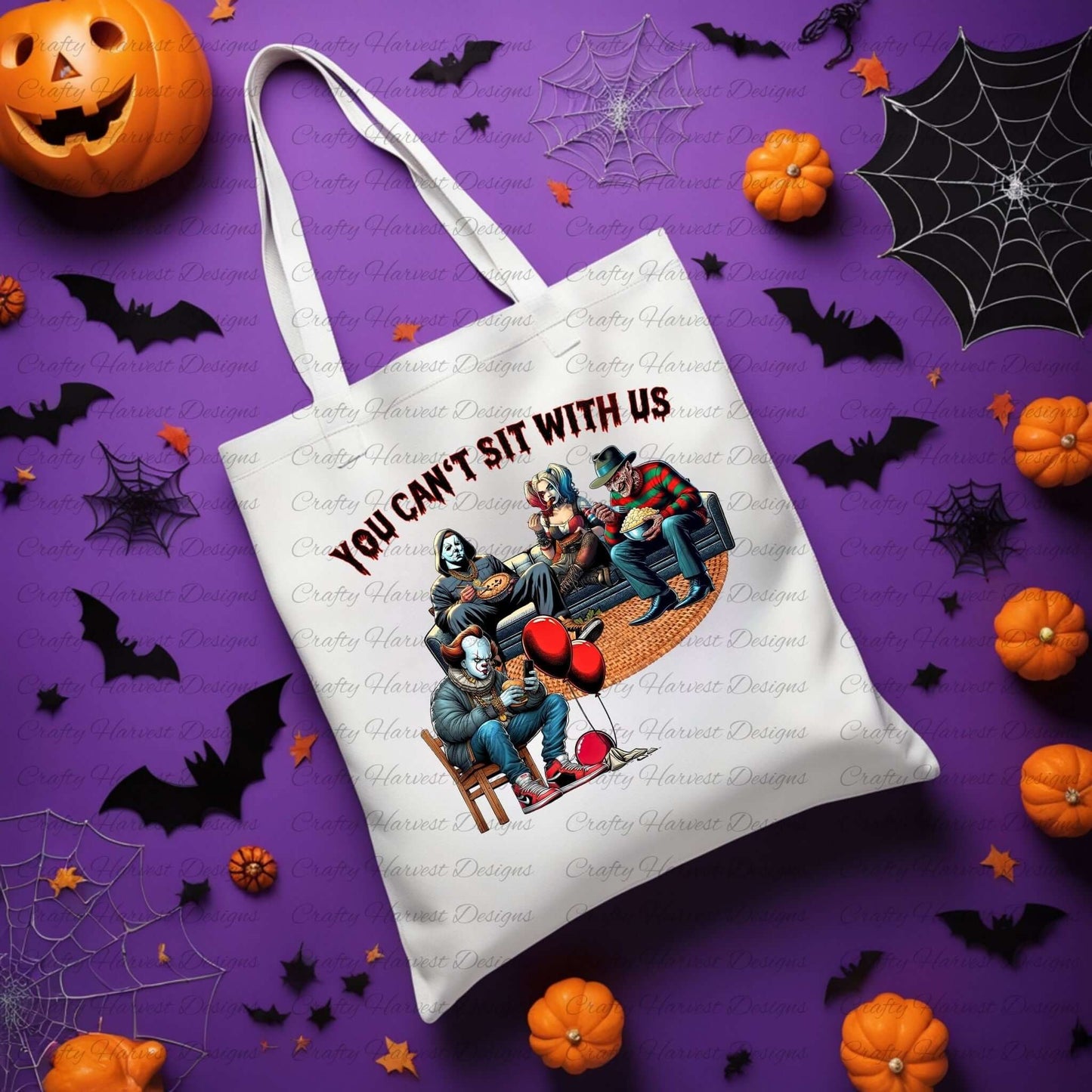 White tote bag featuring the ‘You Can’t Sit With Us’ horror design. Iconic horror characters sit in a humorous scene with bold text above, displayed on a Halloween-themed background with bats, pumpkins, and spiderwebs.