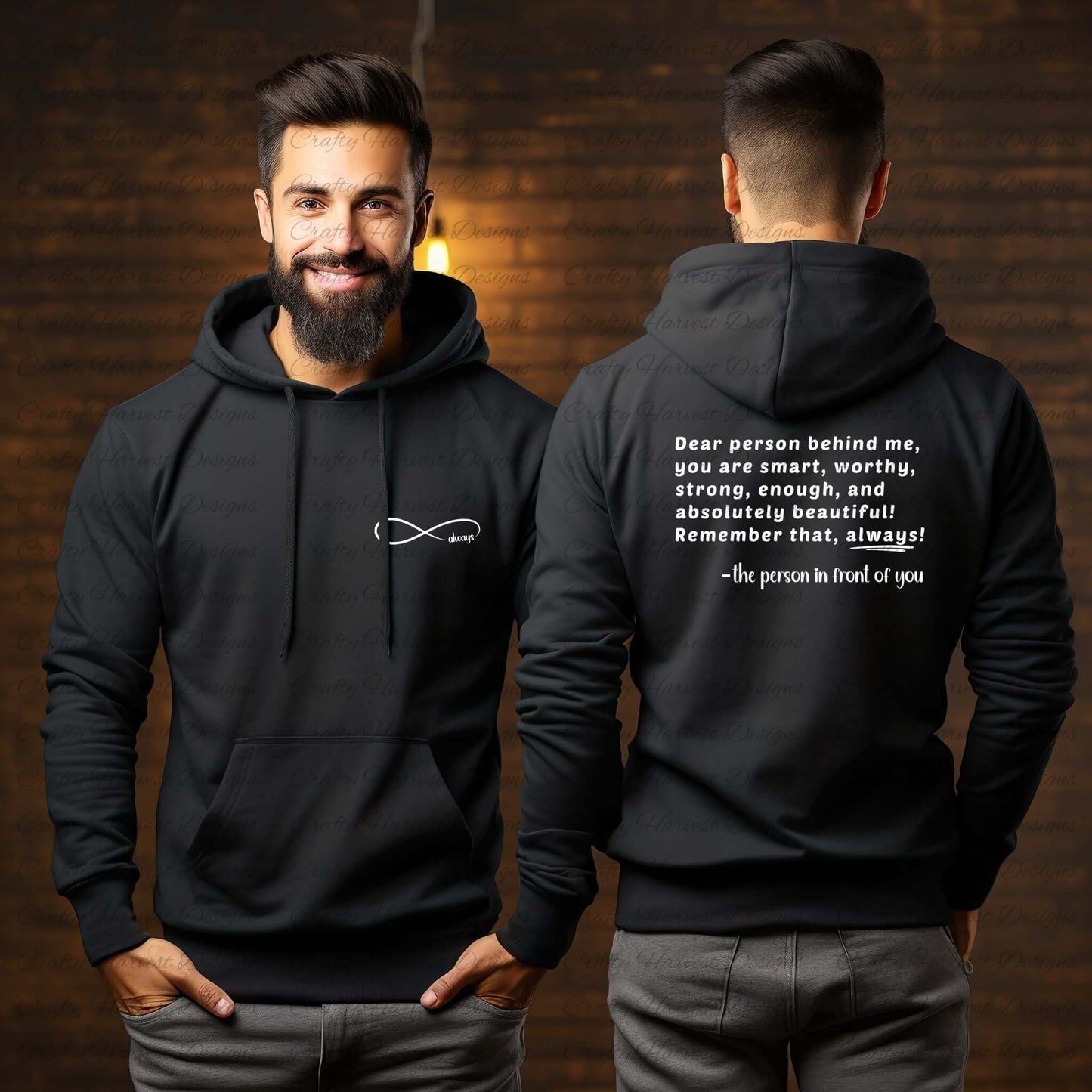 Model wearing a black hoodie featuring the “Dear person behind me” design. The front displays an infinity symbol with the word “always” on the left chest pocket area in white text. The back shows the quote: “Dear person behind me, you are smart, worthy, strong, enough, and absolutely beautiful! Remember that, always! –the person in front of you” in white text. The model is smiling in a warm, indoor setting with soft lighting.