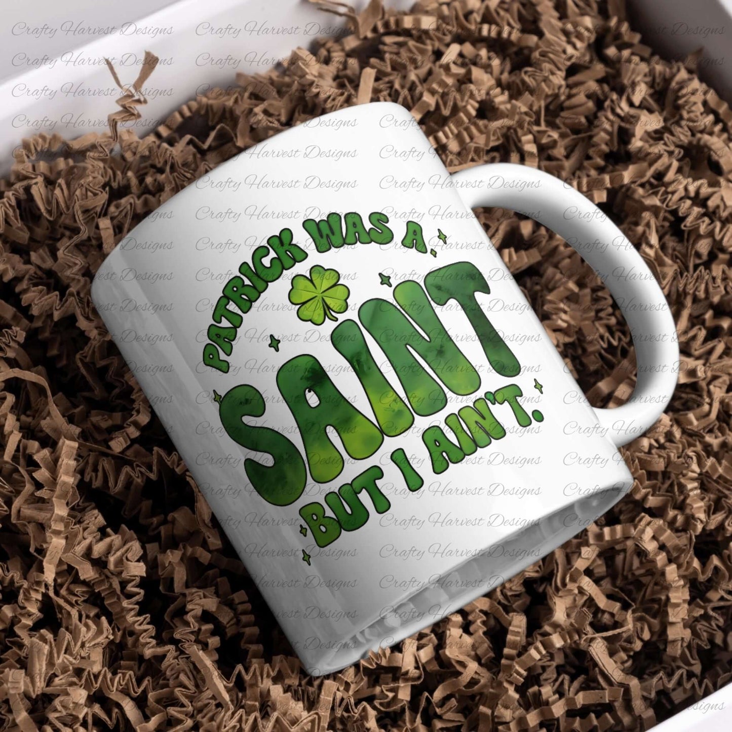 White ceramic mug featuring the St. Patrick’s Day phrase ‘Patrick Was a Saint, But I Ain’t’ in bold green lettering with a shamrock accent. The mug is placed in a gift box with brown crinkle paper, showcasing the design for sublimation or custom printing. PNG and PDF download available.