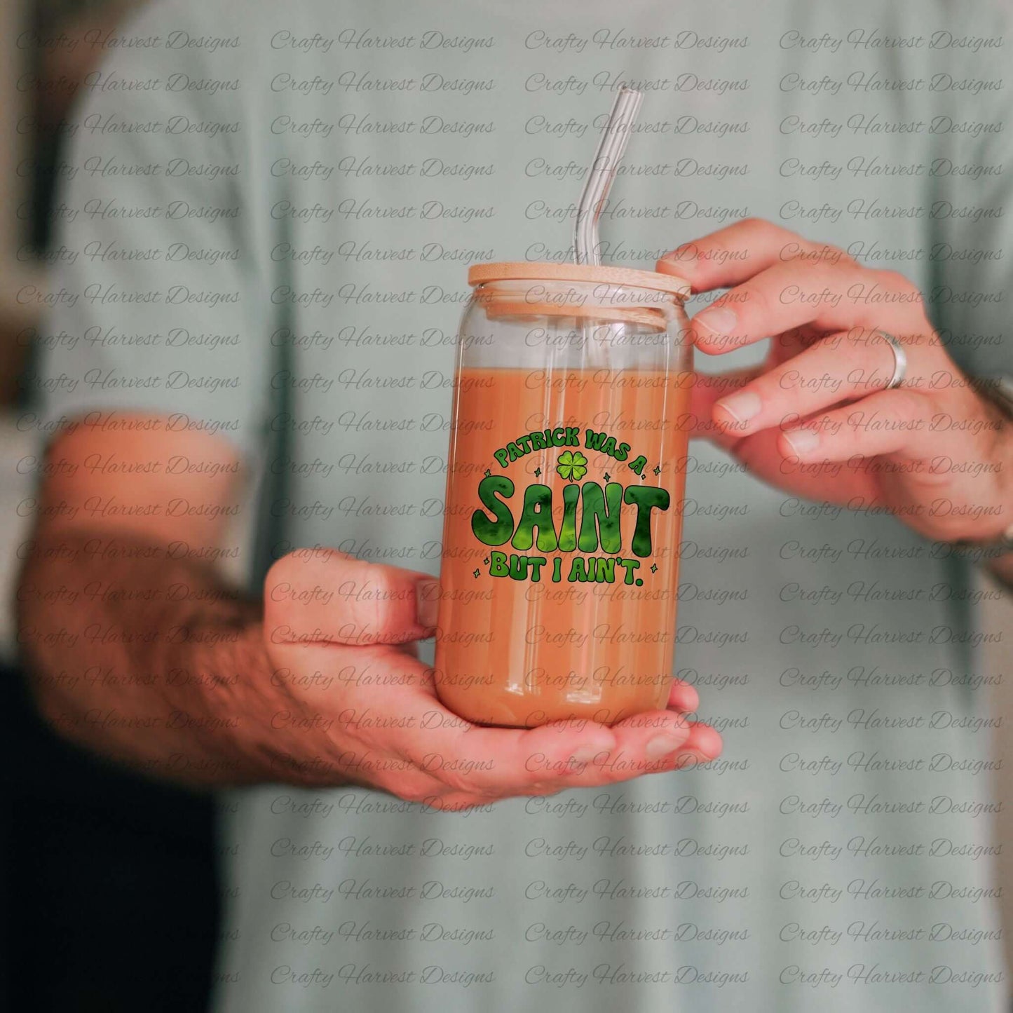 Person holding a glass can with a bamboo lid and straw, featuring the St. Patrick’s Day phrase ‘Patrick Was a Saint, But I Ain’t’ in bold green lettering with a shamrock accent. The drink inside the glass has a light brown color, showcasing how the design appears on drinkware. PNG and PDF download available.