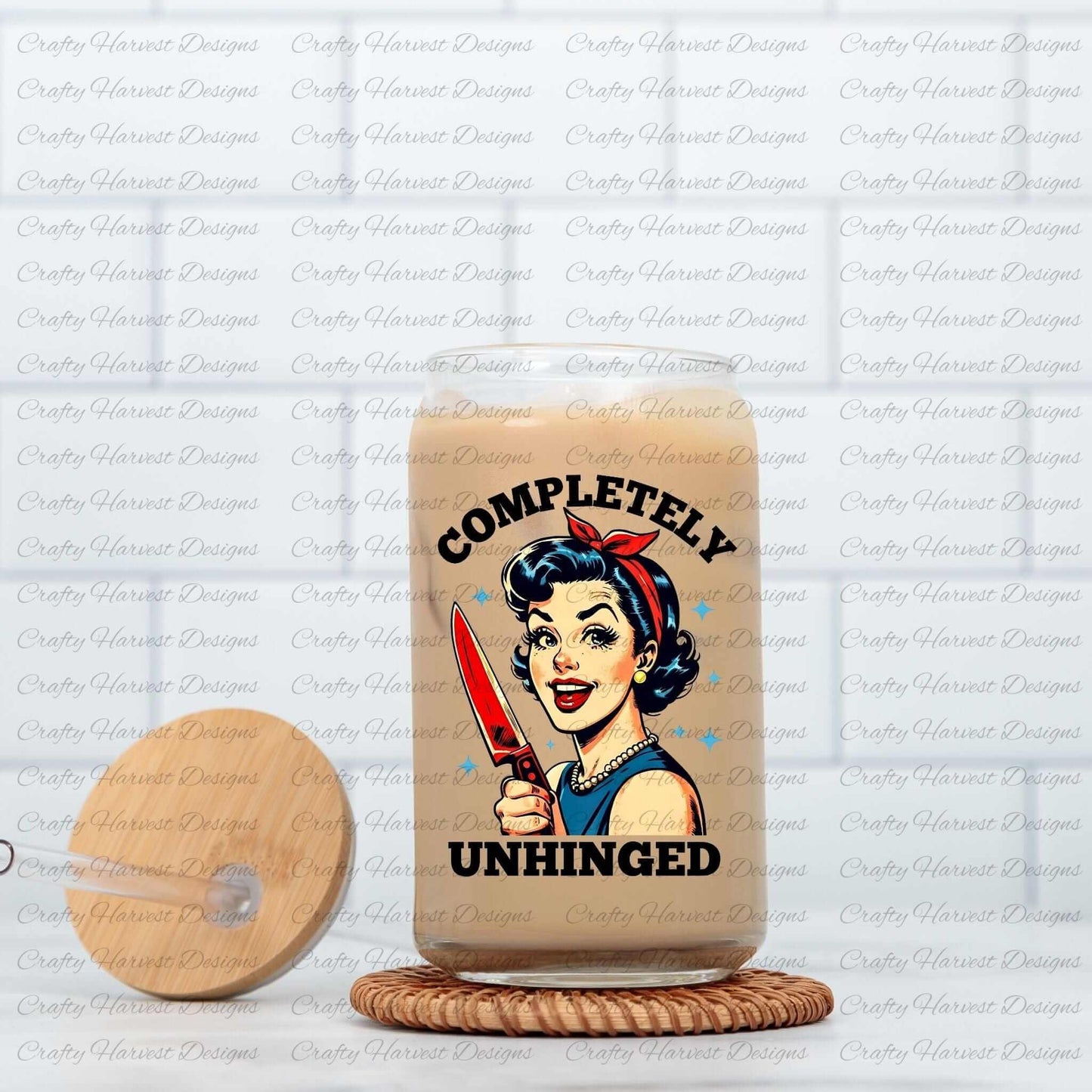 Clear glass can featuring a retro-inspired digital design of a cheerful woman holding a red-handled knife, accompanied by the bold text ‘Completely Unhinged.’ The glass can is displayed on a woven coaster with a matching wooden lid featuring a straw slot, showcasing its use as a stylish and humorous beverage container.