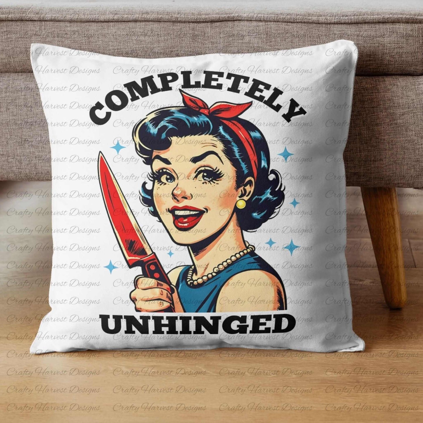 White throw pillow featuring a retro-inspired digital design of a cheerful woman holding a red-handled knife, accompanied by the bold text ‘Completely Unhinged.’ The pillow is displayed on a wooden floor beside a sofa, showcasing its use as a humorous and stylish home decor item.