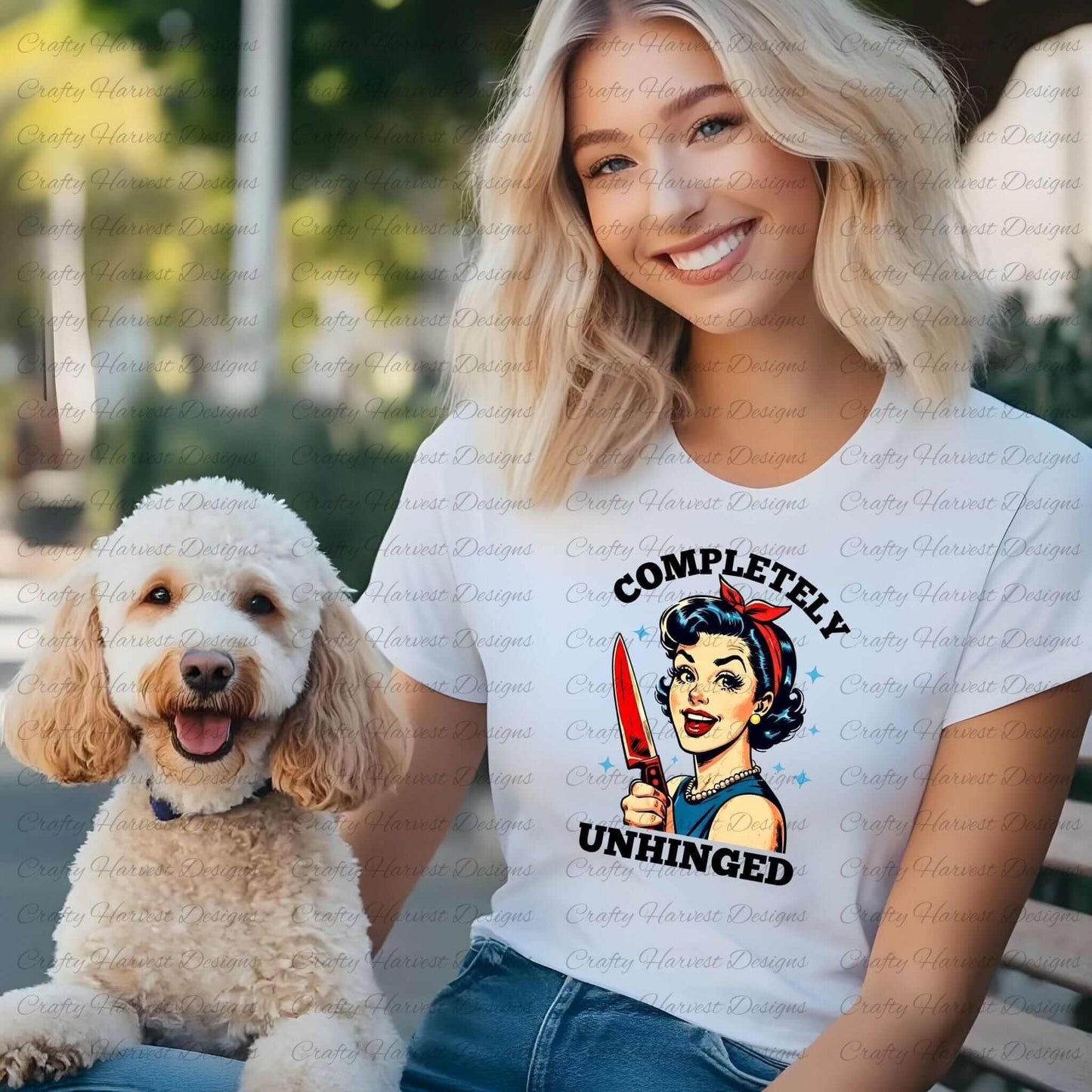 Smiling woman wearing a white t-shirt featuring a retro-inspired digital design of a cheerful woman holding a red-handled knife, accompanied by the bold text ‘Completely Unhinged.’ She is sitting outdoors next to a fluffy white dog, showcasing the design as a playful and stylish apparel option.
