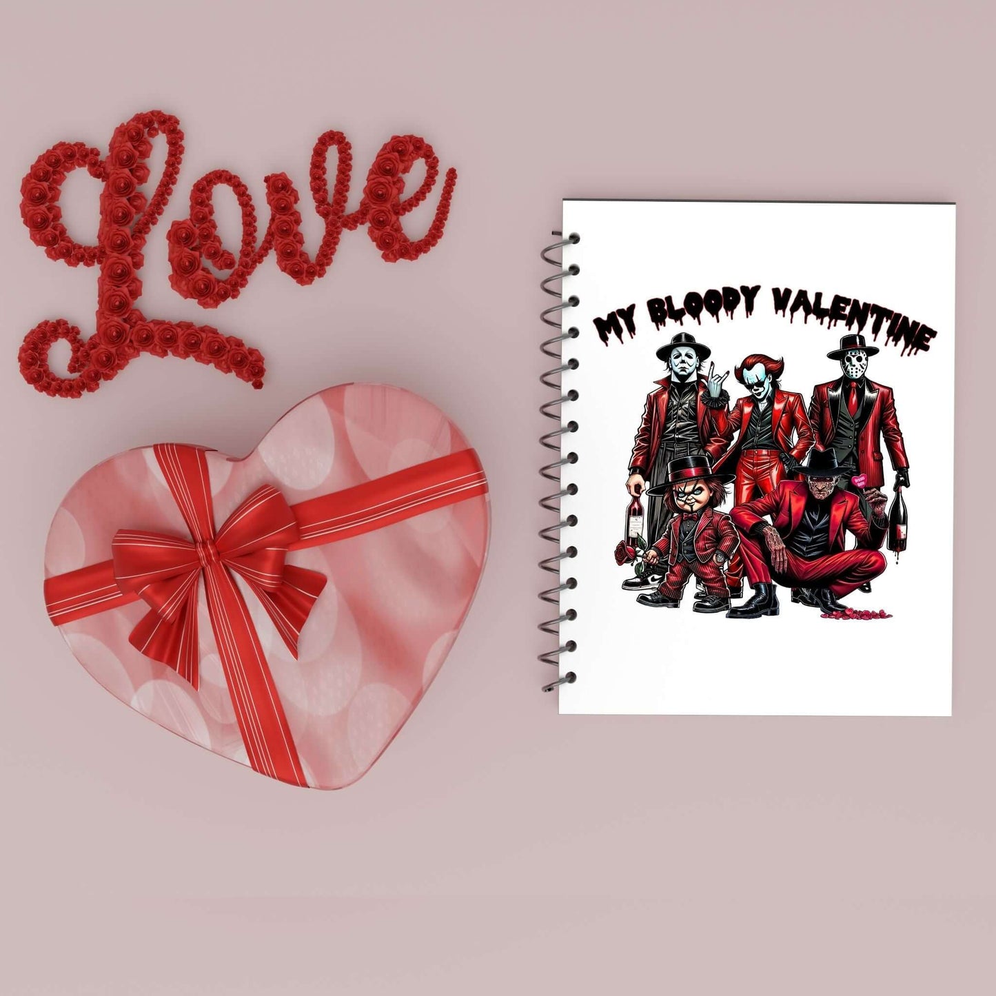 Flat lay featuring a spiral notebook with a horror-themed Valentine’s Day design titled “My Bloody Valentine,” alongside a heart-shaped gift box with a red ribbon and a decorative “Love” sign made of red roses on a light pink background.