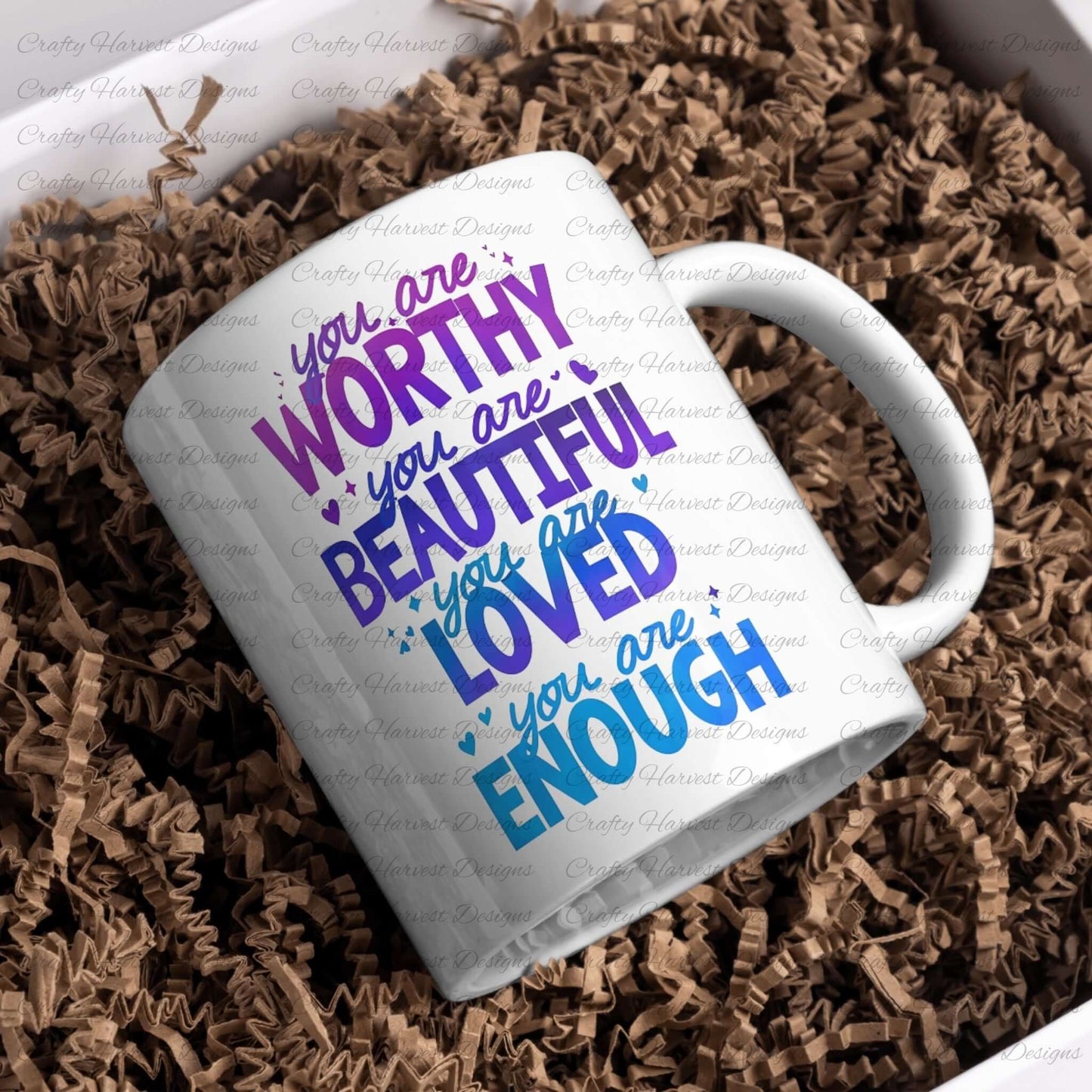 White ceramic mug featuring the motivational phrase ‘You are Worthy, Beautiful, Loved, Enough’ in purple and blue gradient text, placed in a box filled with brown shredded paper.
