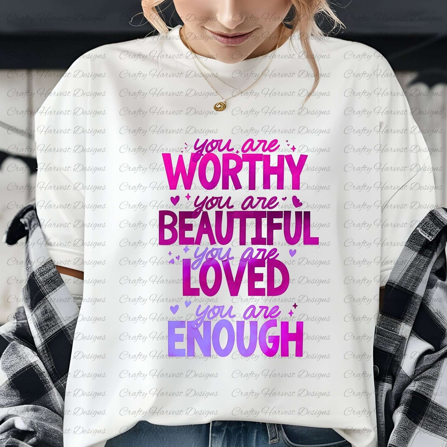 Close-up of a woman wearing a white t-shirt featuring the motivational phrase ‘You are Worthy, Beautiful, Loved, Enough’ in a gradient of pink and purple text with heart accents, layered with a black-and-white flannel shirt.
