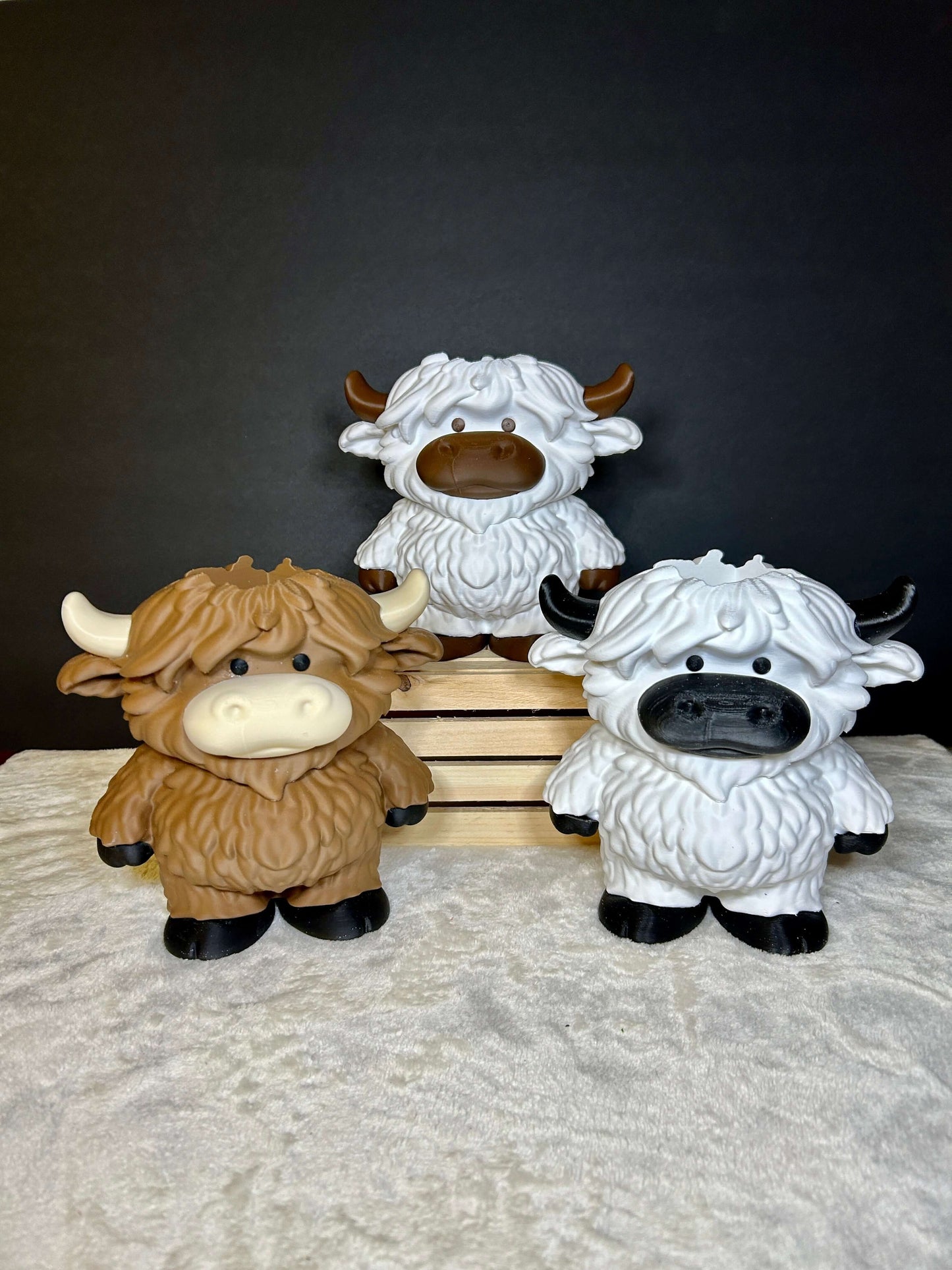 Three highland cow soap dispensers on a textured surface with a dark background