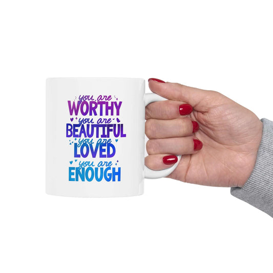 a hand holding a ceramic white mug with the quote "you are worthy, you are beautiful, you are loved, you are enough".