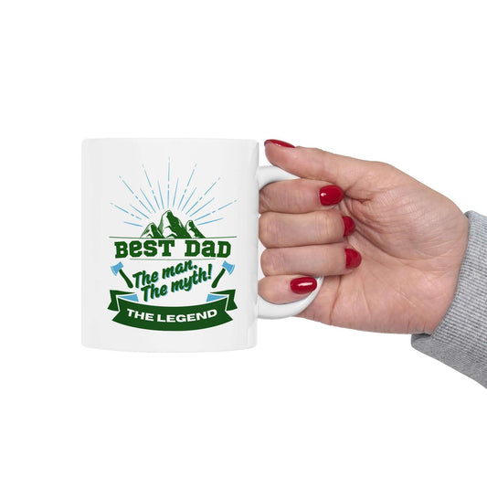 hand holding a white ceramic mug featuring a graphic design with green and blue text and decorative accents.