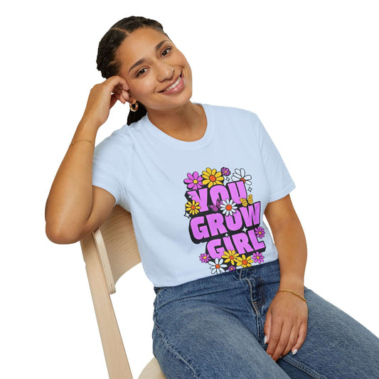 Woman wearing a light blue t-shirt displaying the phrase ‘YOU GROW GIRL’ in bold purple letters surrounded by colorful flowers.