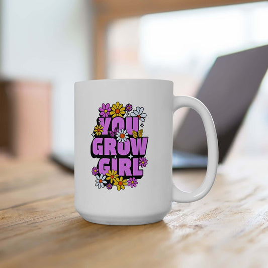 White ceramic mug placed on a wooden table, featuring the text ‘YOU GROW GIRL’ in bold purple letters surrounded by colorful flowers.