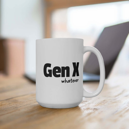 A white ceramic coffee mug featuring the phrase “Gen X whatever” in bold black text. The mug is placed on a wooden surface with a blurred background showing a laptop, creating a casual and modern setting.