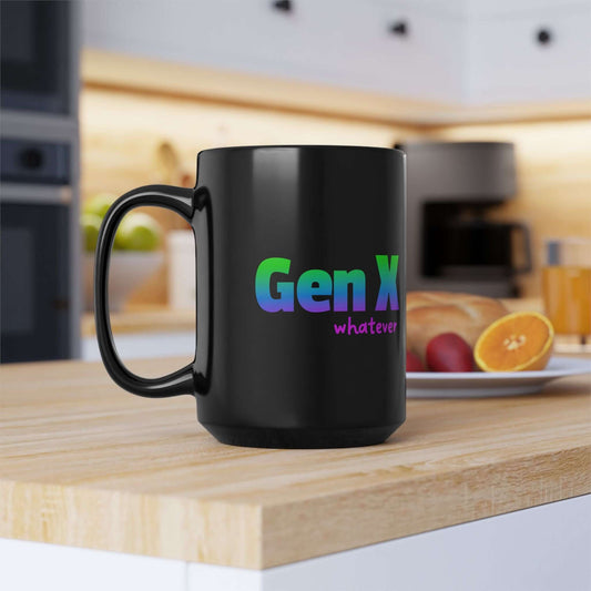A black ceramic coffee mug featuring the phrase “Gen X whatever” in a bold gradient of blue, green, and purple text. The mug sits on a wooden kitchen counter with a blurred background of a coffee maker and a plate of fresh fruit, creating a cozy and modern setting.