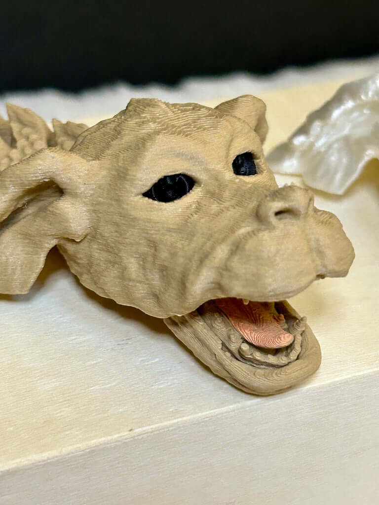 3D-printed dragon head model on a light surface with a dark background