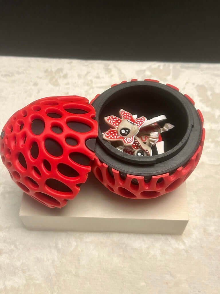 Red and black textured ball with a small decorative item inside on a light gray surface.